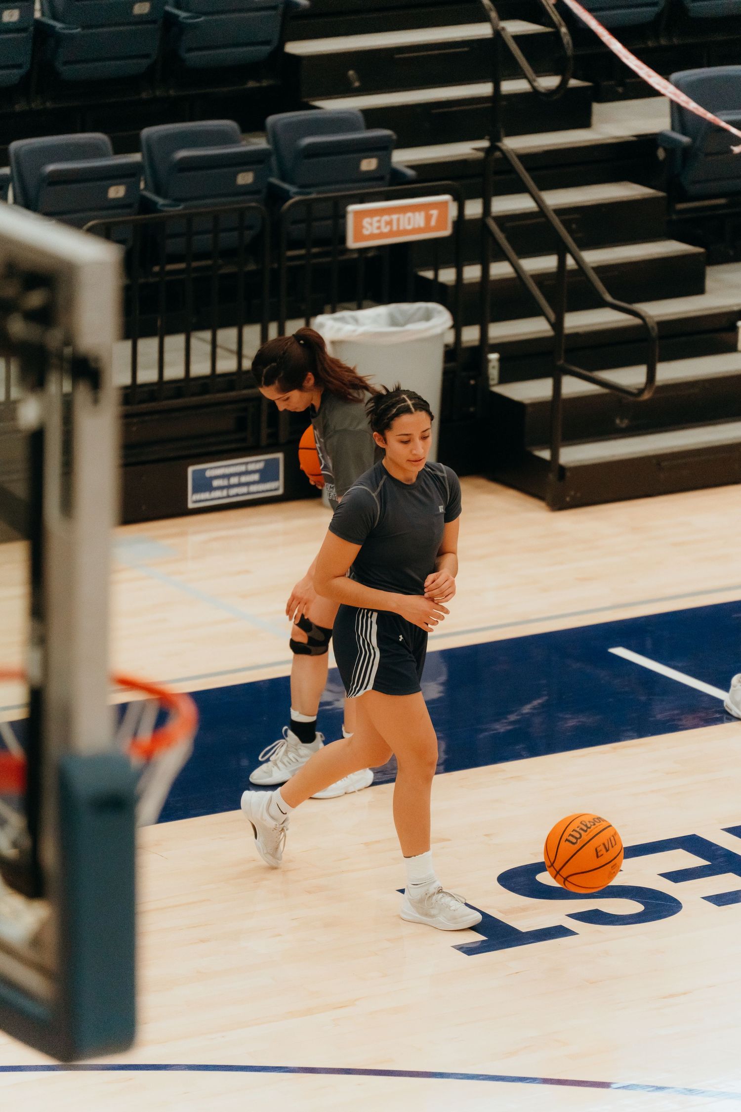Basketball players practicing on indoor court near stadium seating.