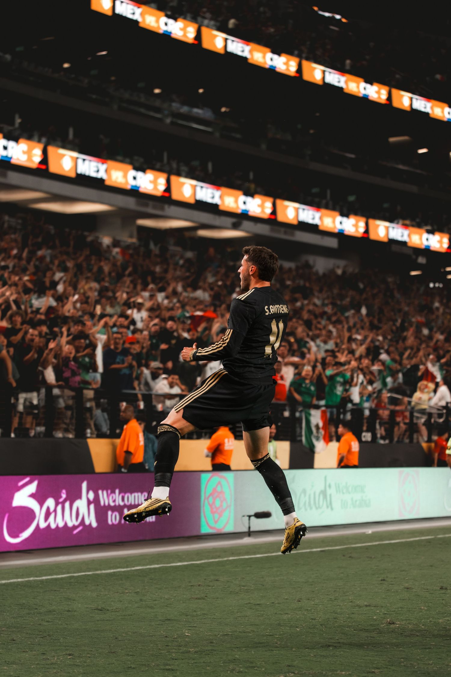 Soccer player in black uniform leaps for joy during celebration in front of cheering stadium crowd.