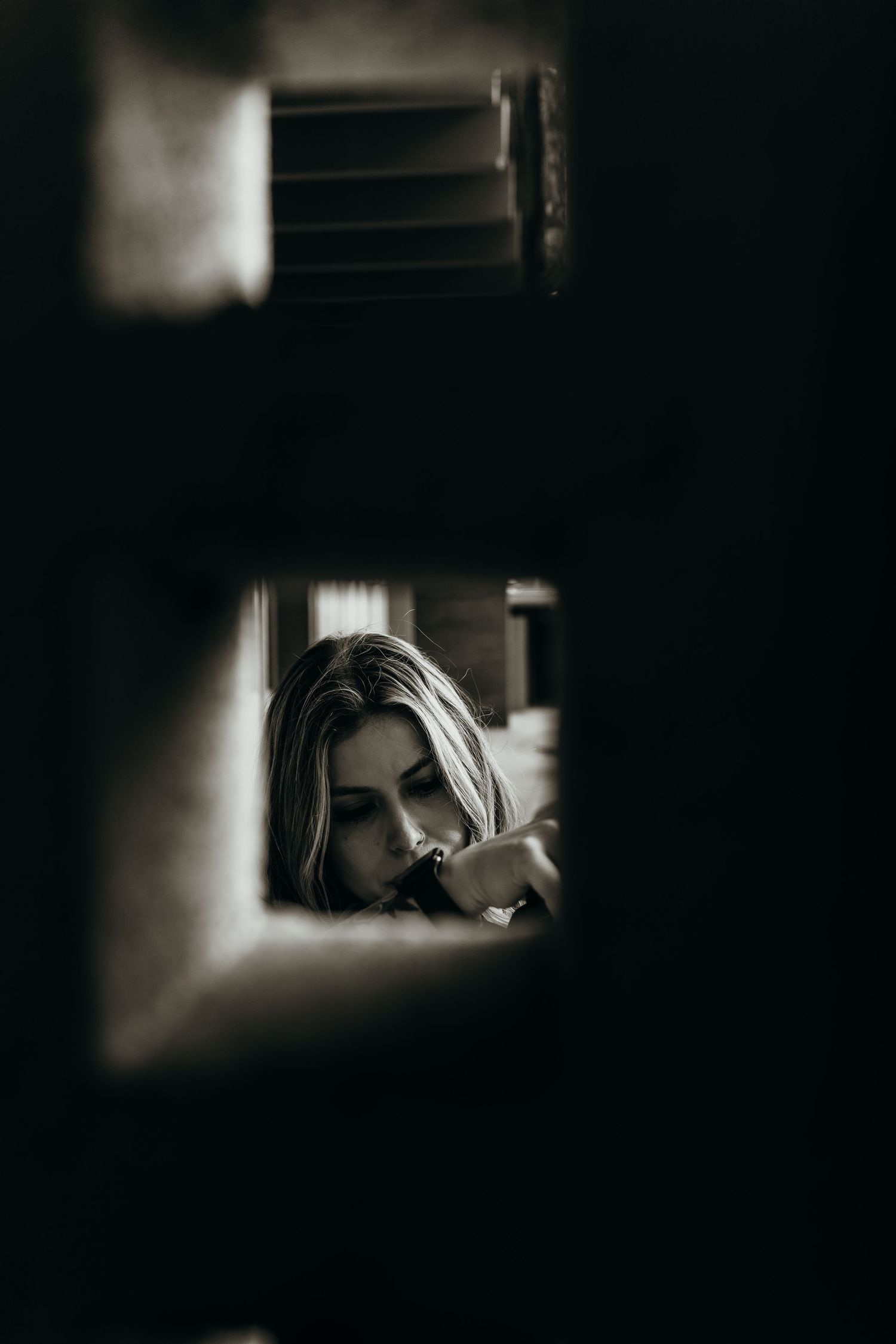 Artistic black and white portrait framed through a small window or opening.