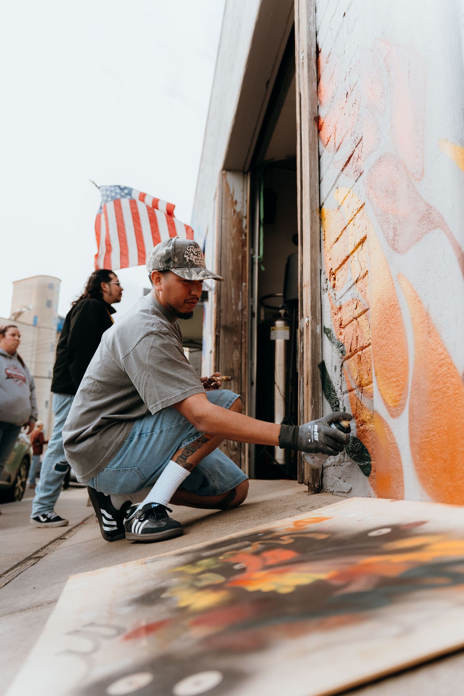Artist creating street art with spray paint while an American flag waves in the background.