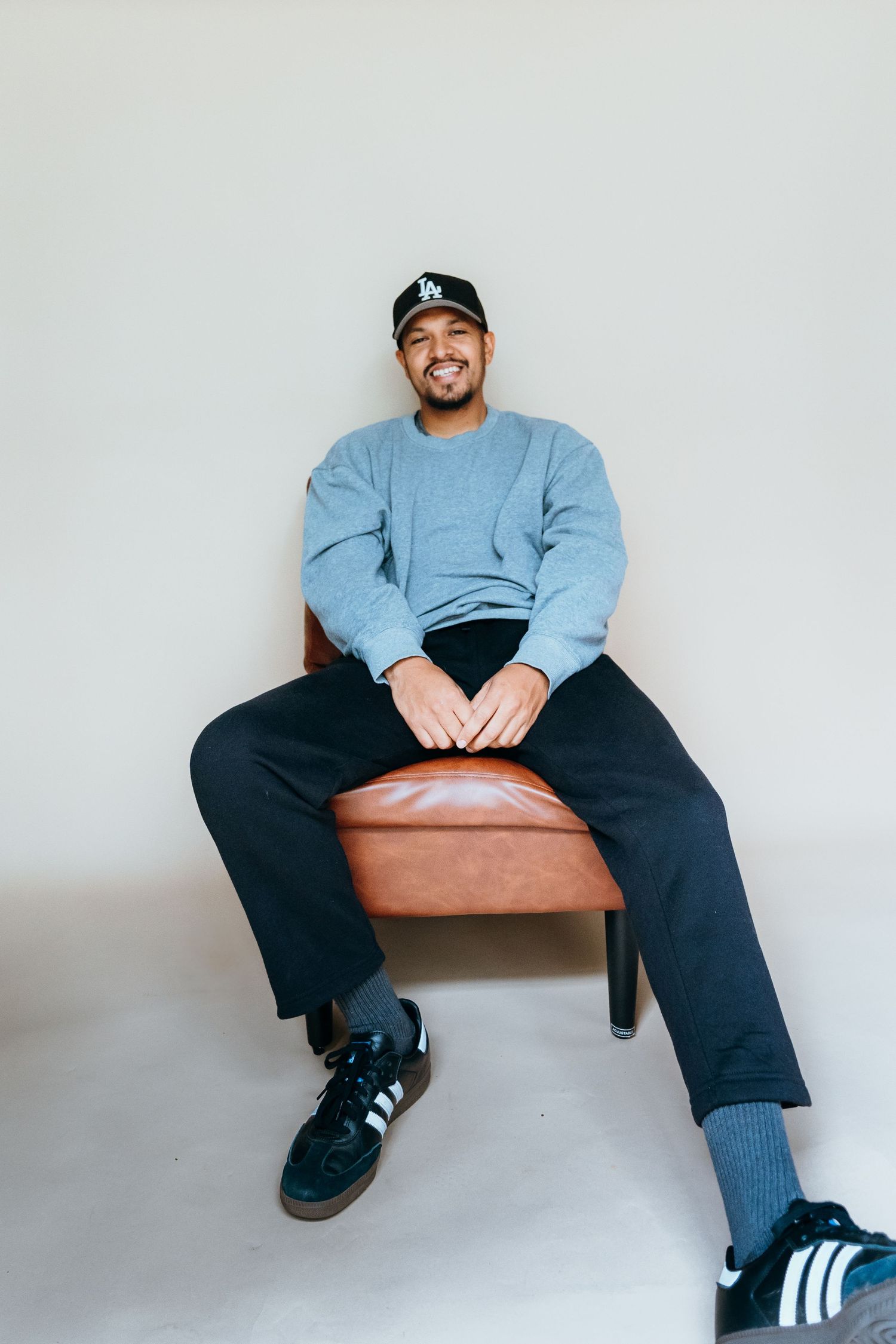 Person in casual blue sweatshirt and cap sits comfortably on brown leather furniture.