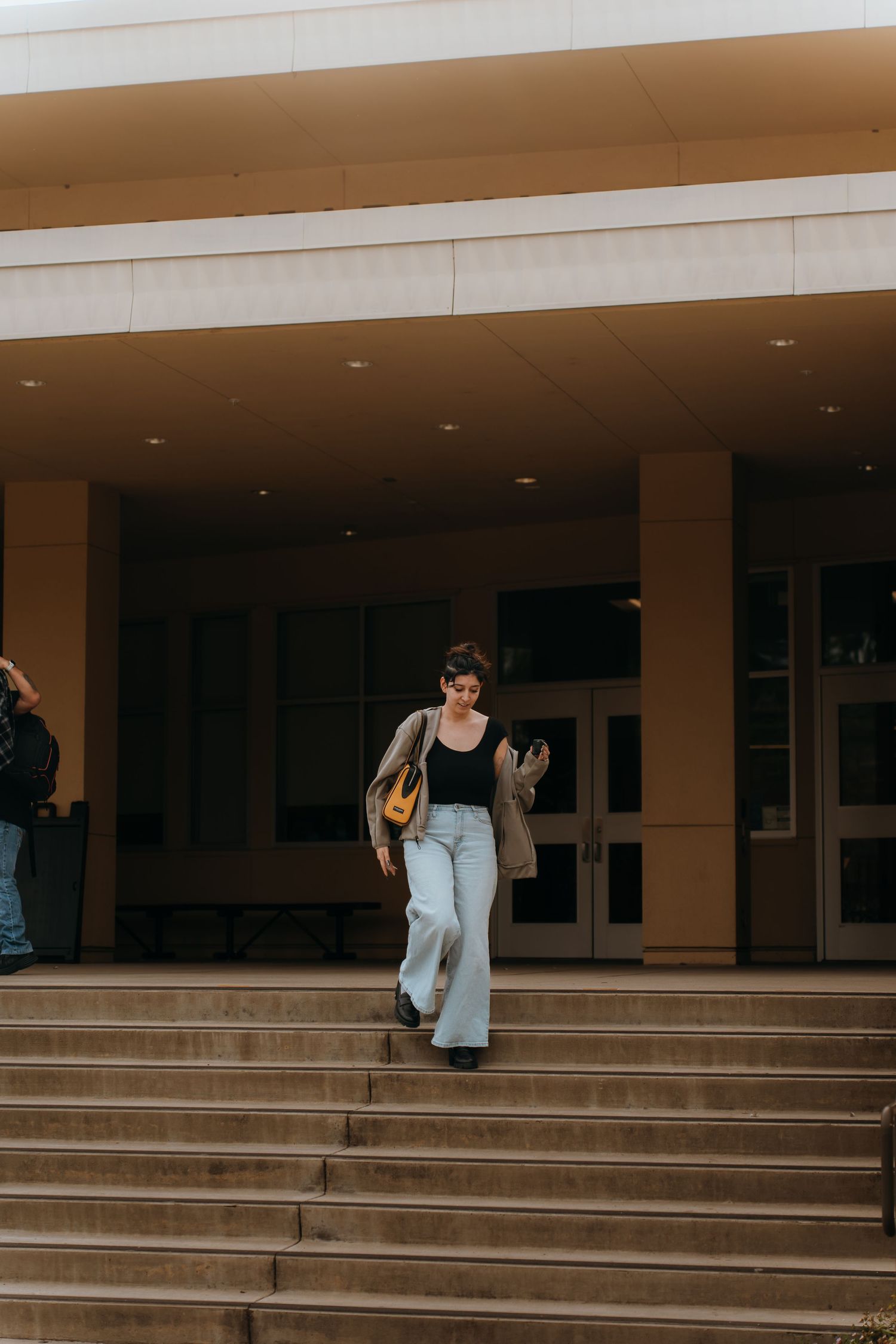 Student walking down steps of a campus building carrying a backpack and books.