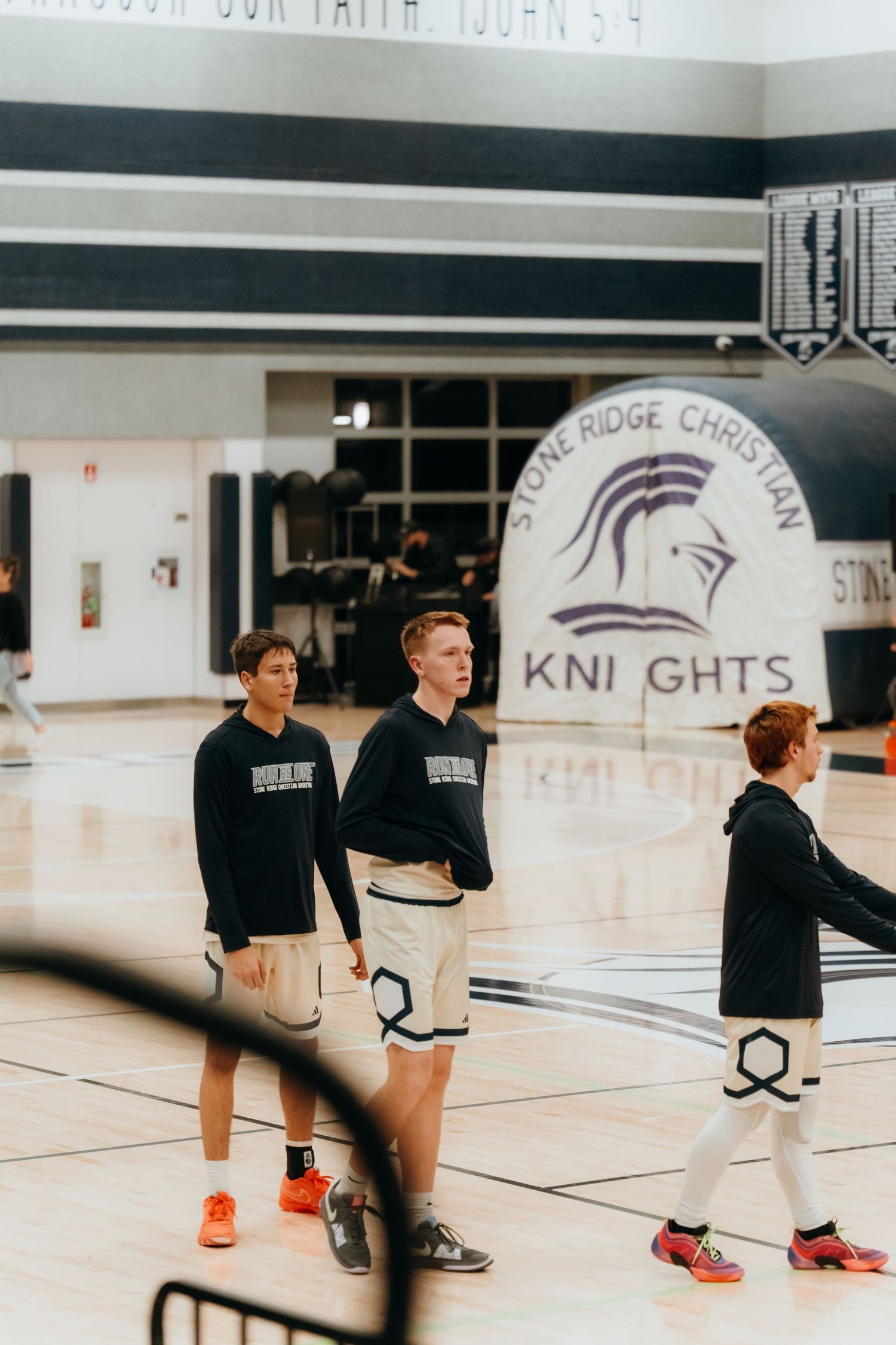 Basketball players gather near Knights logo in school gymnasium during practice.