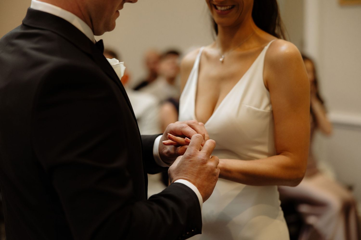 A couple exchanges rings during an intimate wedding ceremony in a light-filled indoor venue.