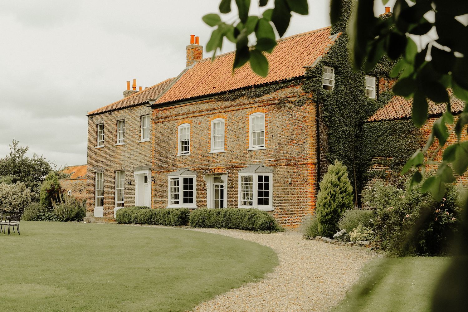 A series of rustic brick farmhouses with traditional architecture line a rural countryside path.