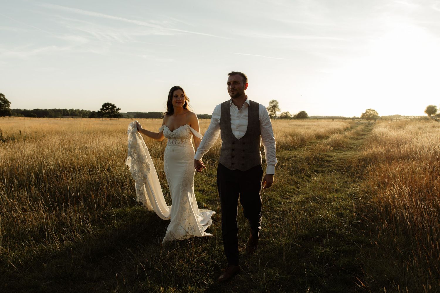 A couple walks together through a golden wheat field at sunset holding hands in romantic countryside setting.