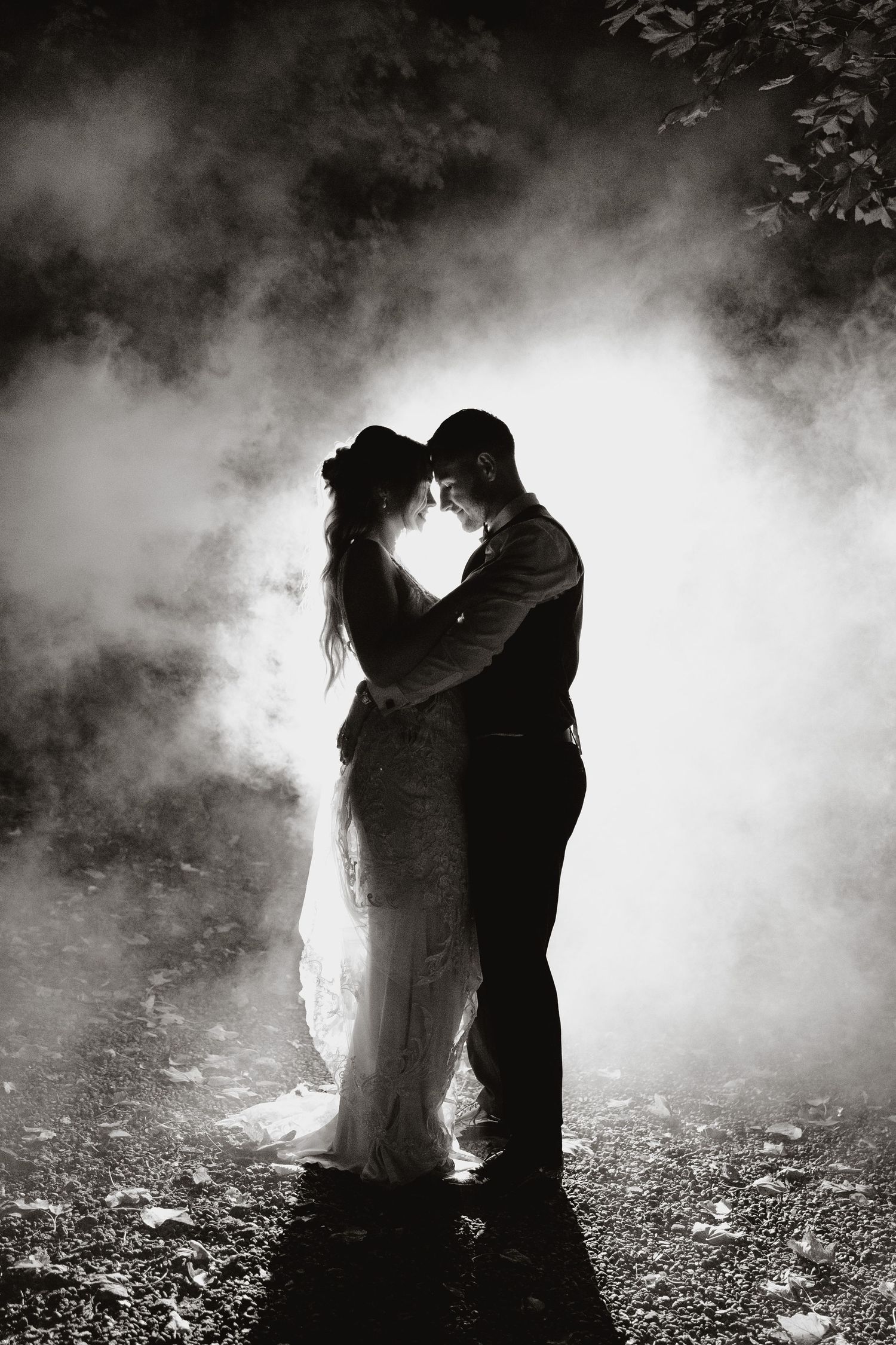 Romantic silhouettes of a couple embrace in misty black and white forest setting creating a dreamy atmospheric scene.