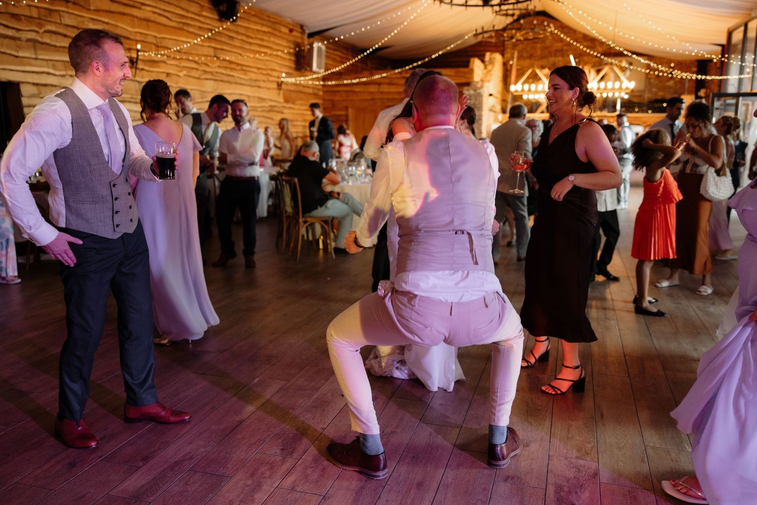 Wedding reception in a rustic barn venue with guests dancing under elegant draping and chandeliers.