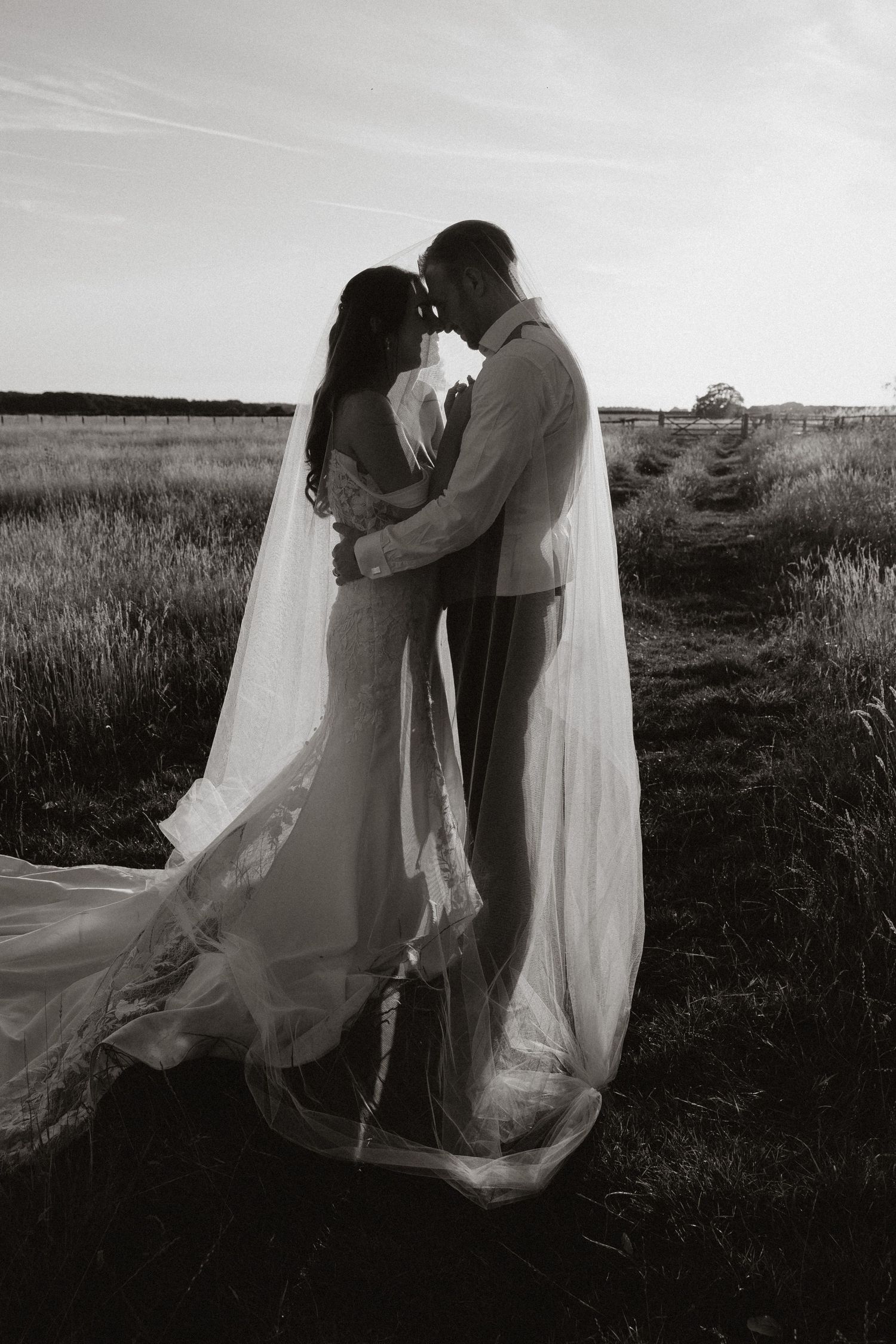 A romantic black and white photo series of a couple in wedding attire embracing in a field at sunset.