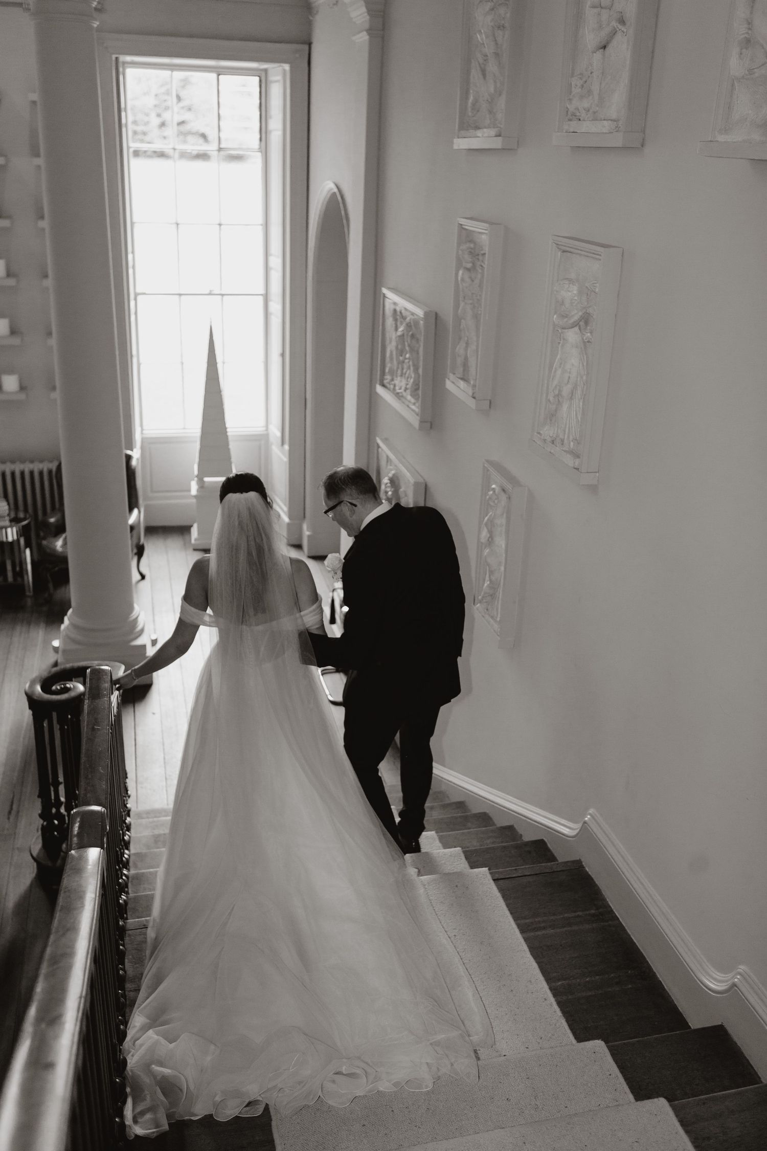 White bridal gown sweeps dramatically through a sunlit hallway with elegant white walls and classical architectural details.