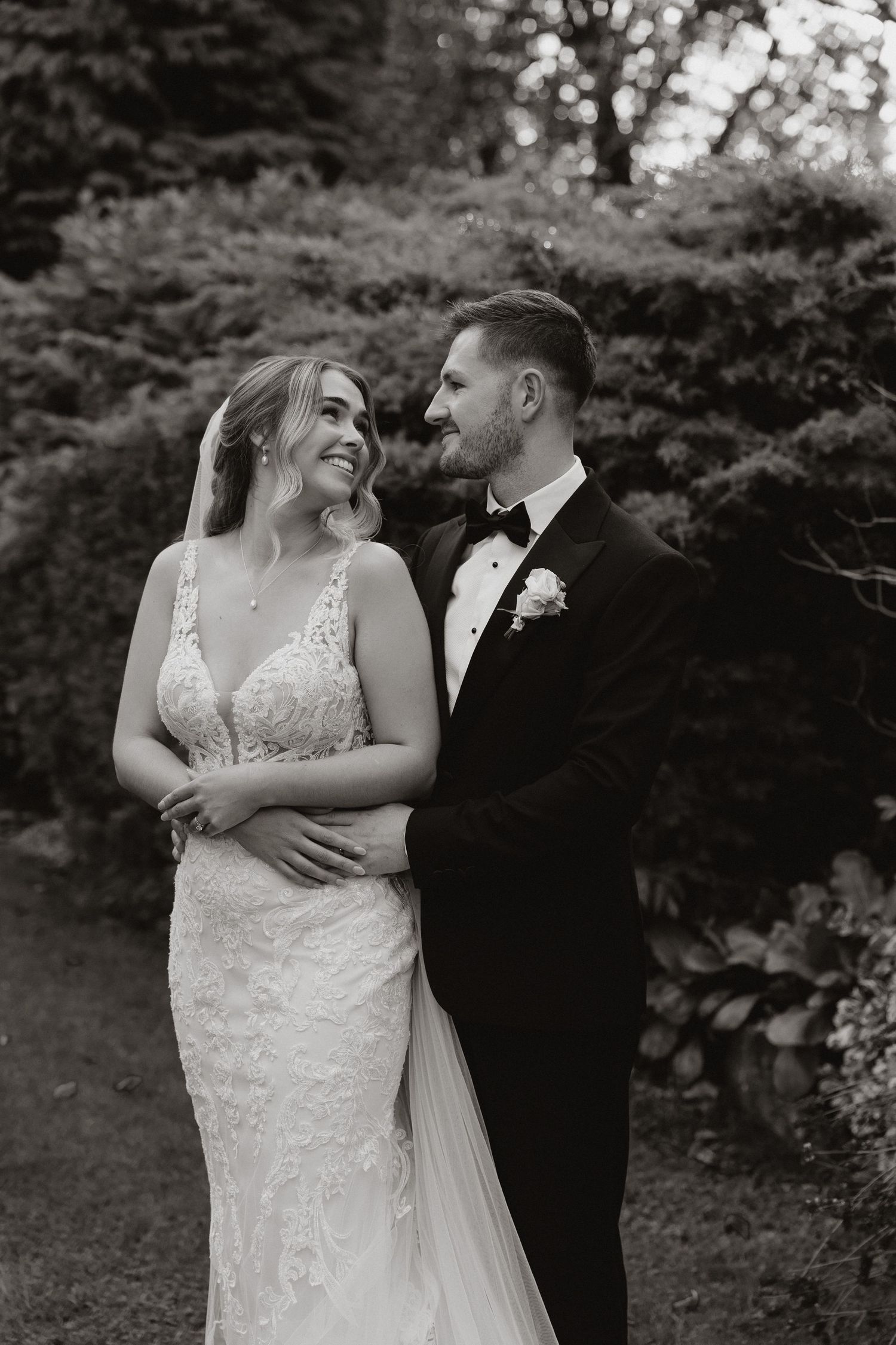 A couple shares an intimate moment while embracing outdoors in black and white wedding attire.