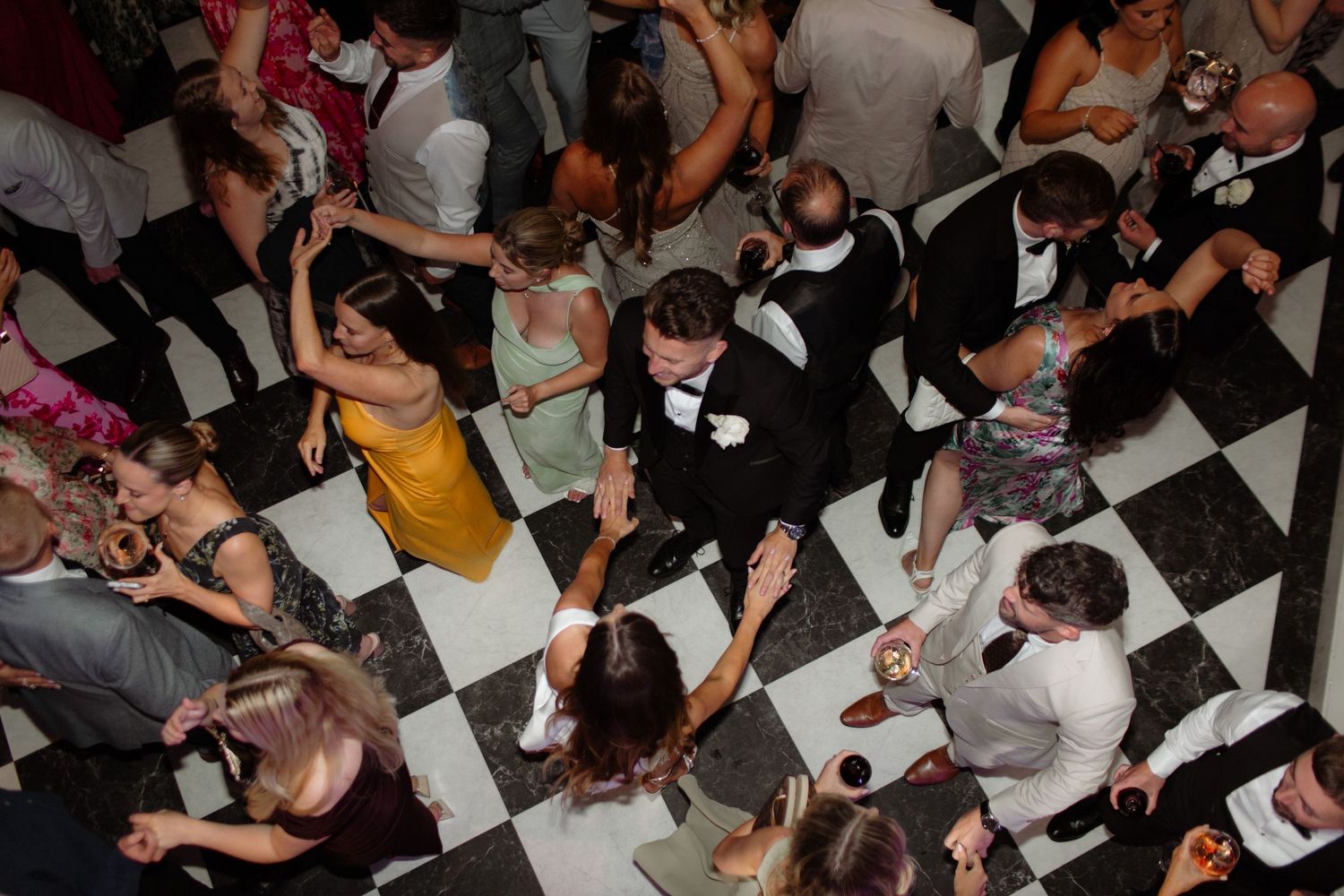 A large crowd of people dancing and socializing on a black and white checkered dance floor at a party.