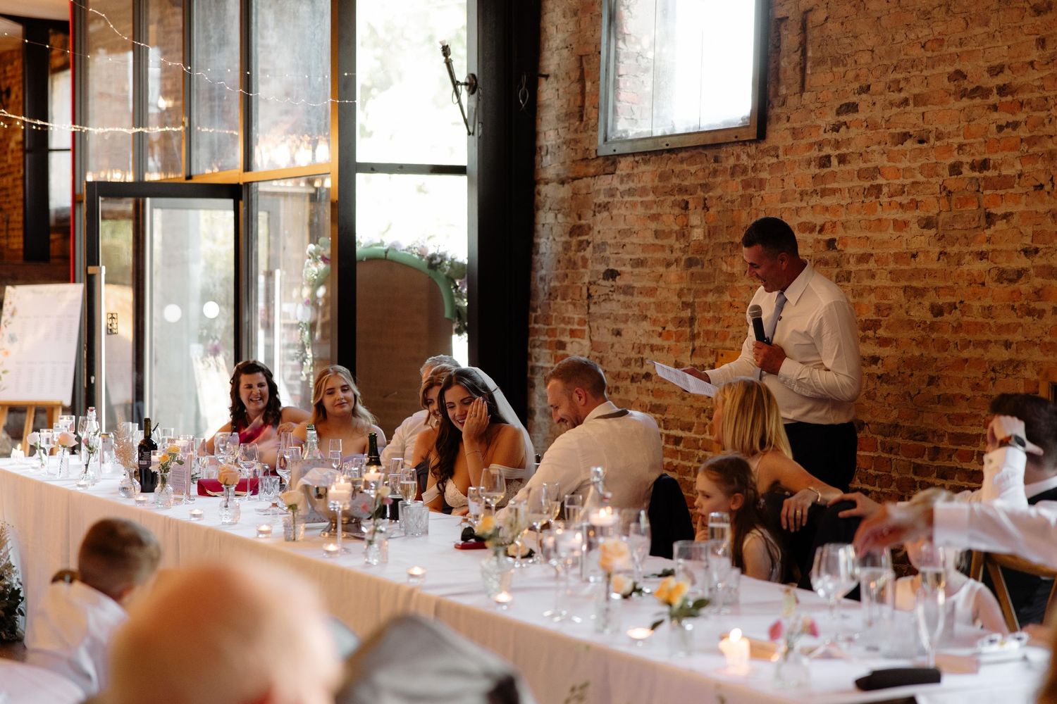 Wedding reception setup in rustic brick venue with long tables and elegant white table settings.