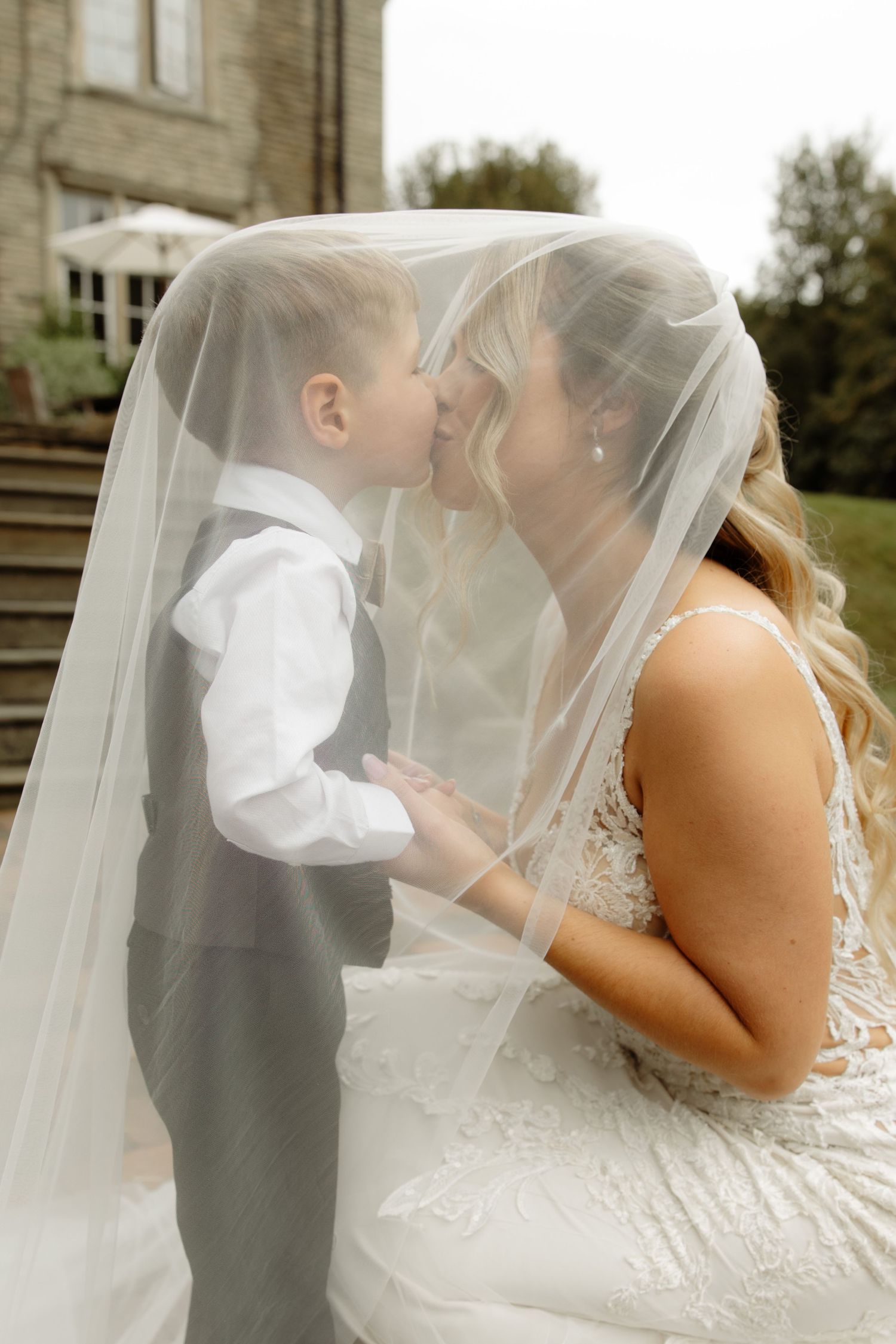 A tender moment shared under a flowing white veil during an outdoor wedding ceremony.
