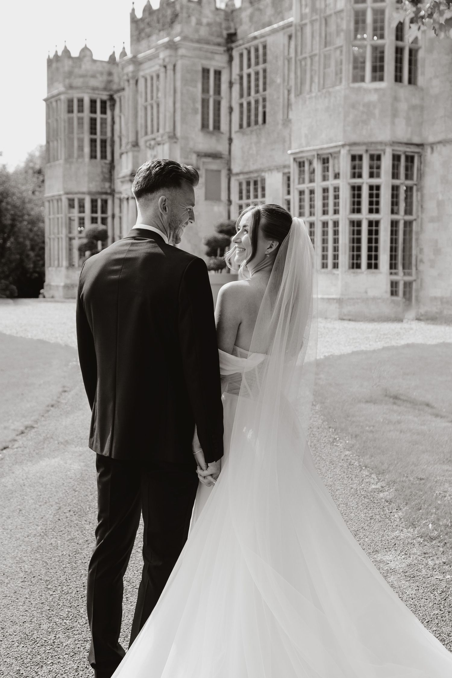 Black and white wedding photos show couple walking away from grand manor house in sequence.