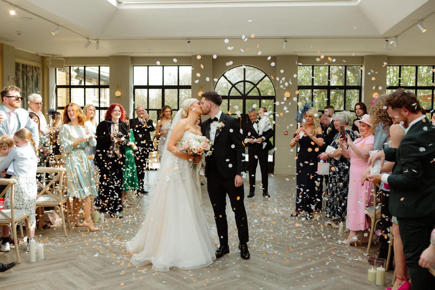 Wedding guests toss confetti at a newly married couple during a joyful exit celebration at an elegant indoor venue.