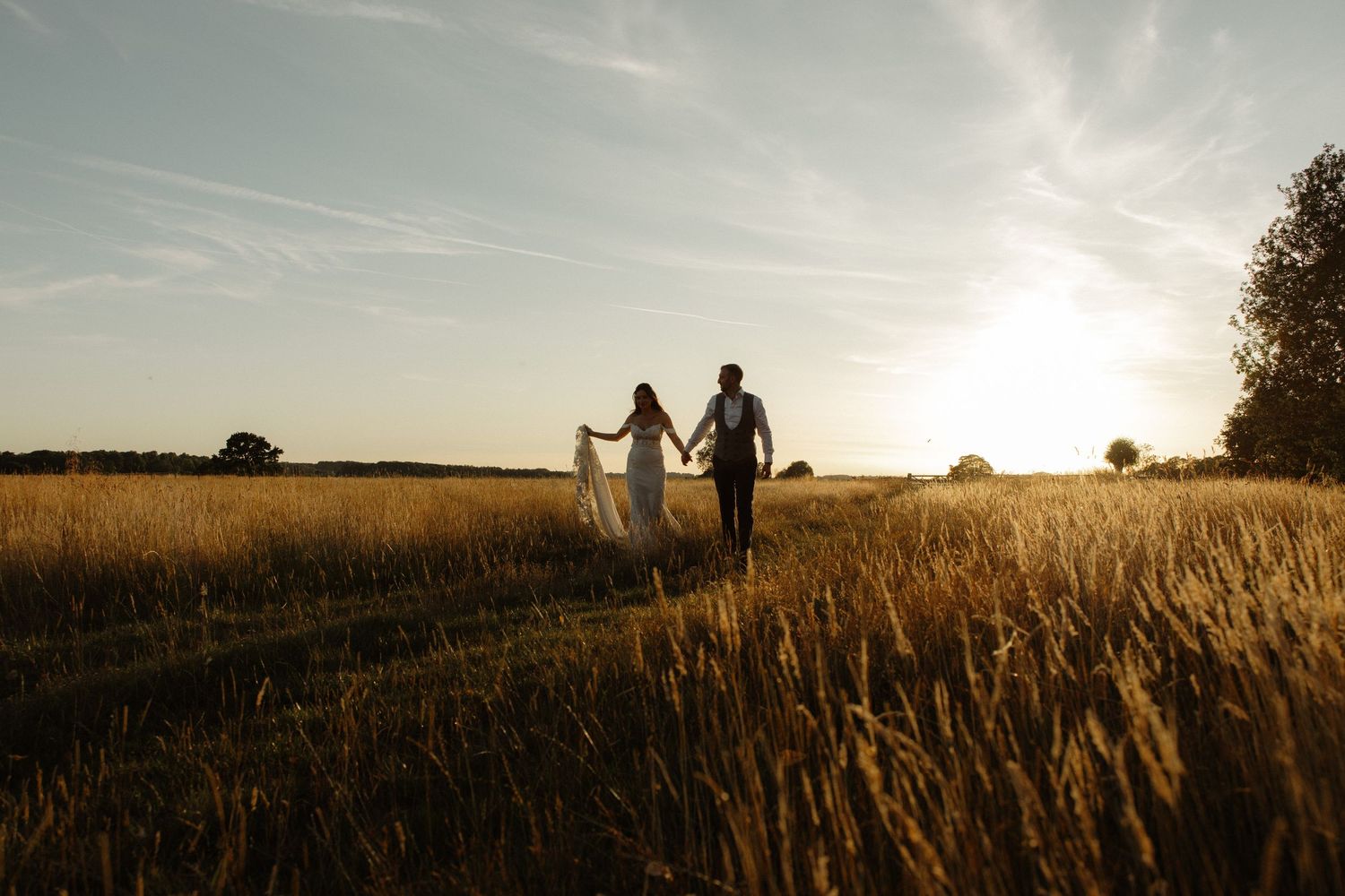 Silhouettes of people walking together through a golden wheat field at sunset against a hazy summer sky.
