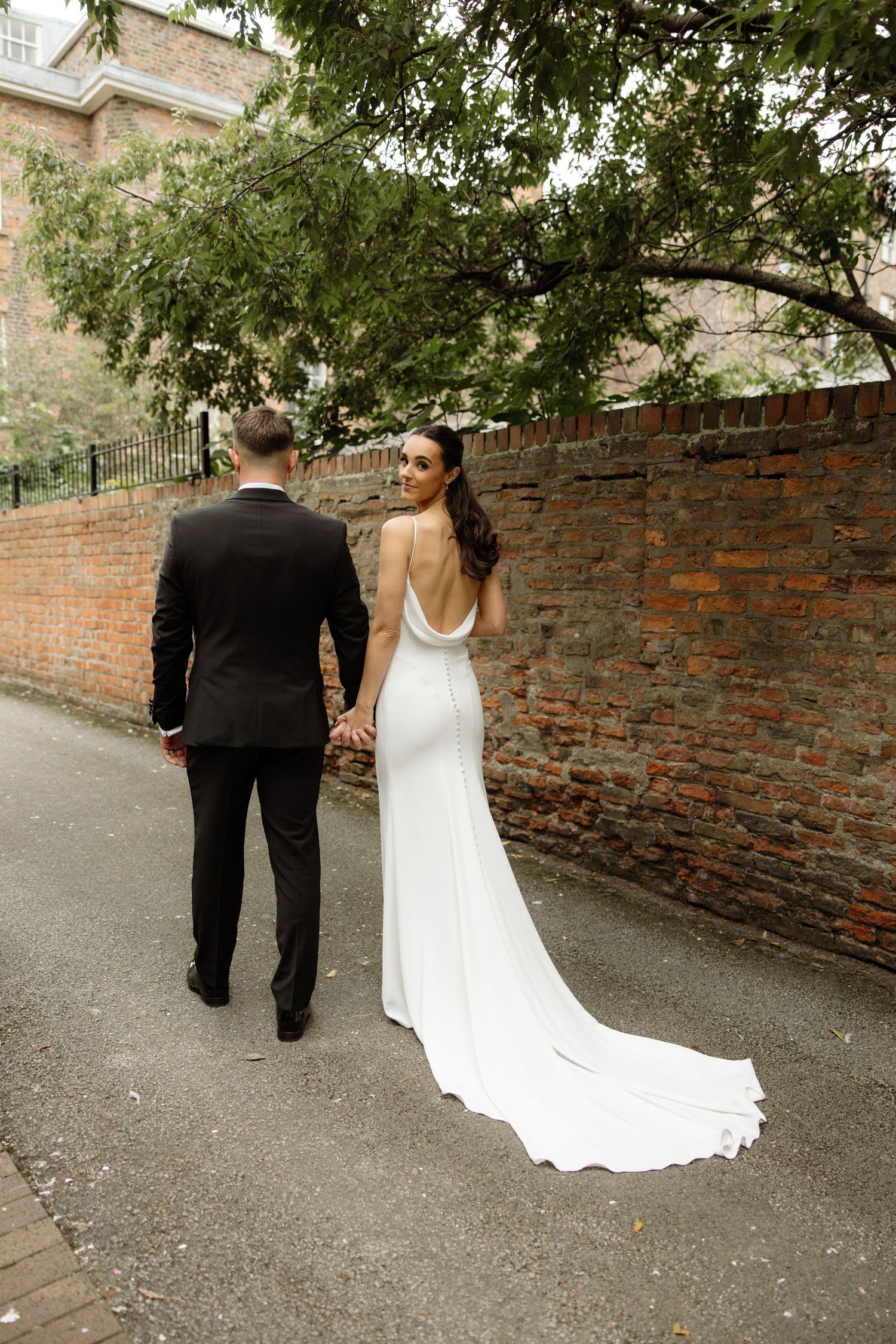 A couple in wedding attire walks together along a brick wall path during their special day.