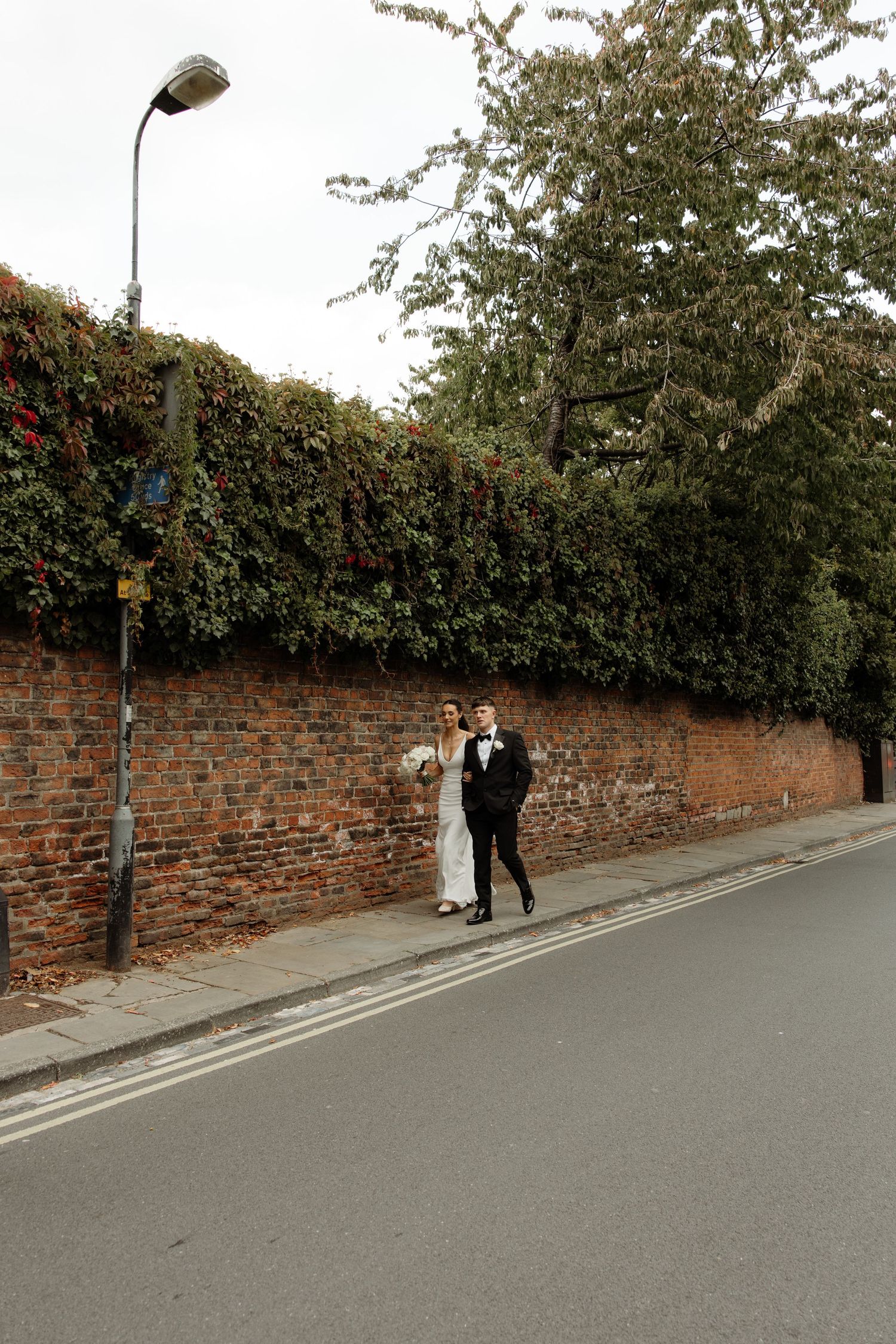 A couple stands against a rustic brick wall on a quiet street during a wedding photo session.