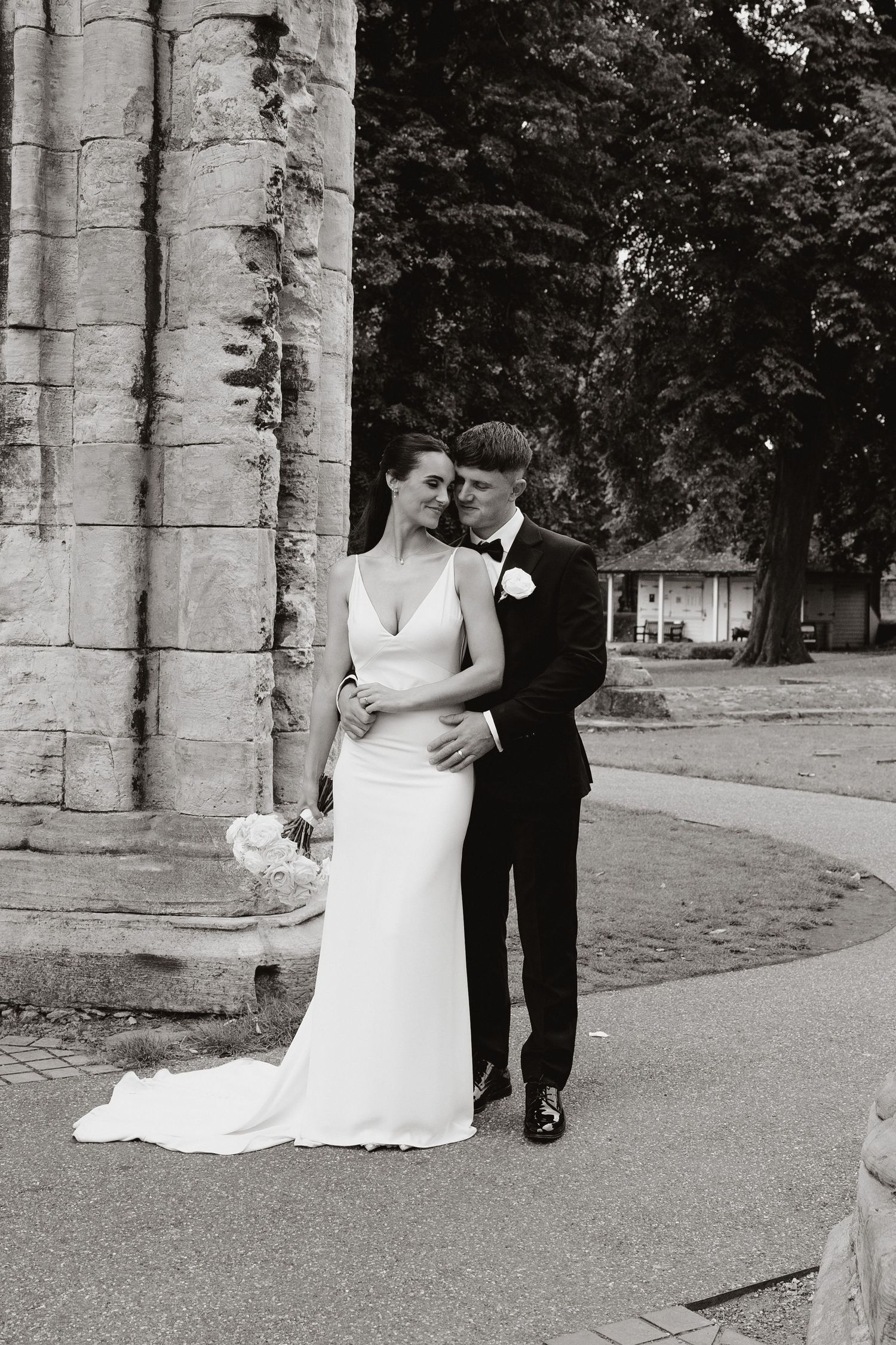 A romantic black and white wedding photo sequence showing a couple dancing together between stone pillars outdoors.