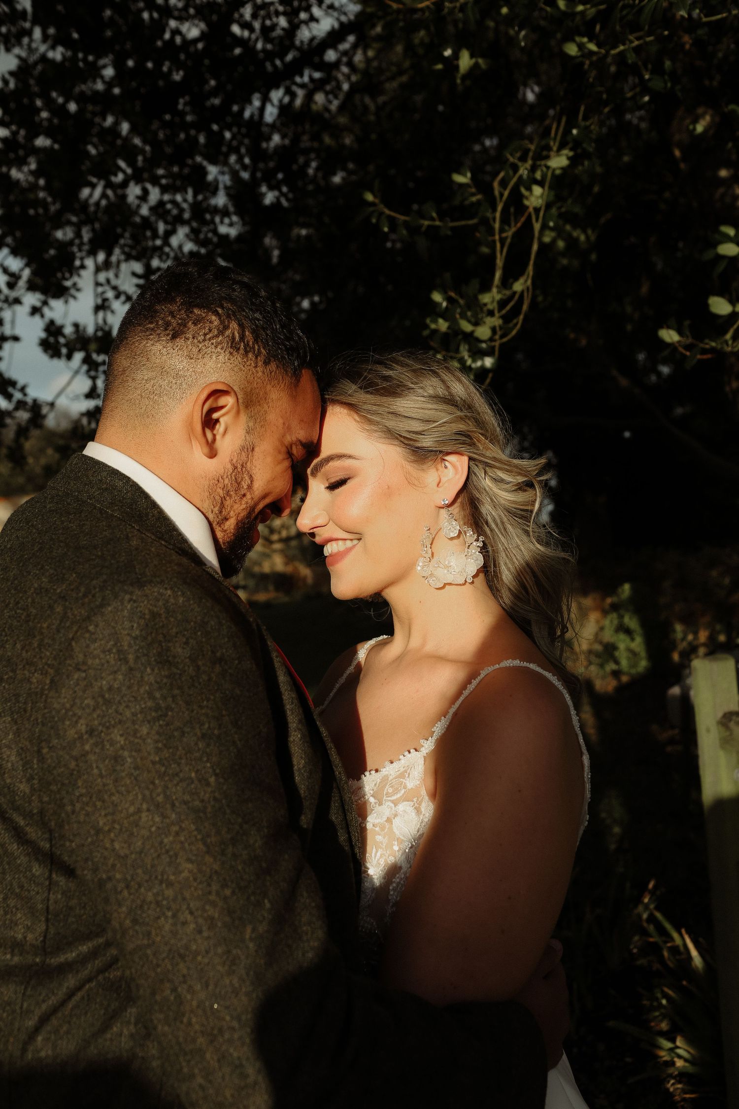Romantic sunset wedding portrait featuring a tender moment between newlyweds in rustic outdoor setting.