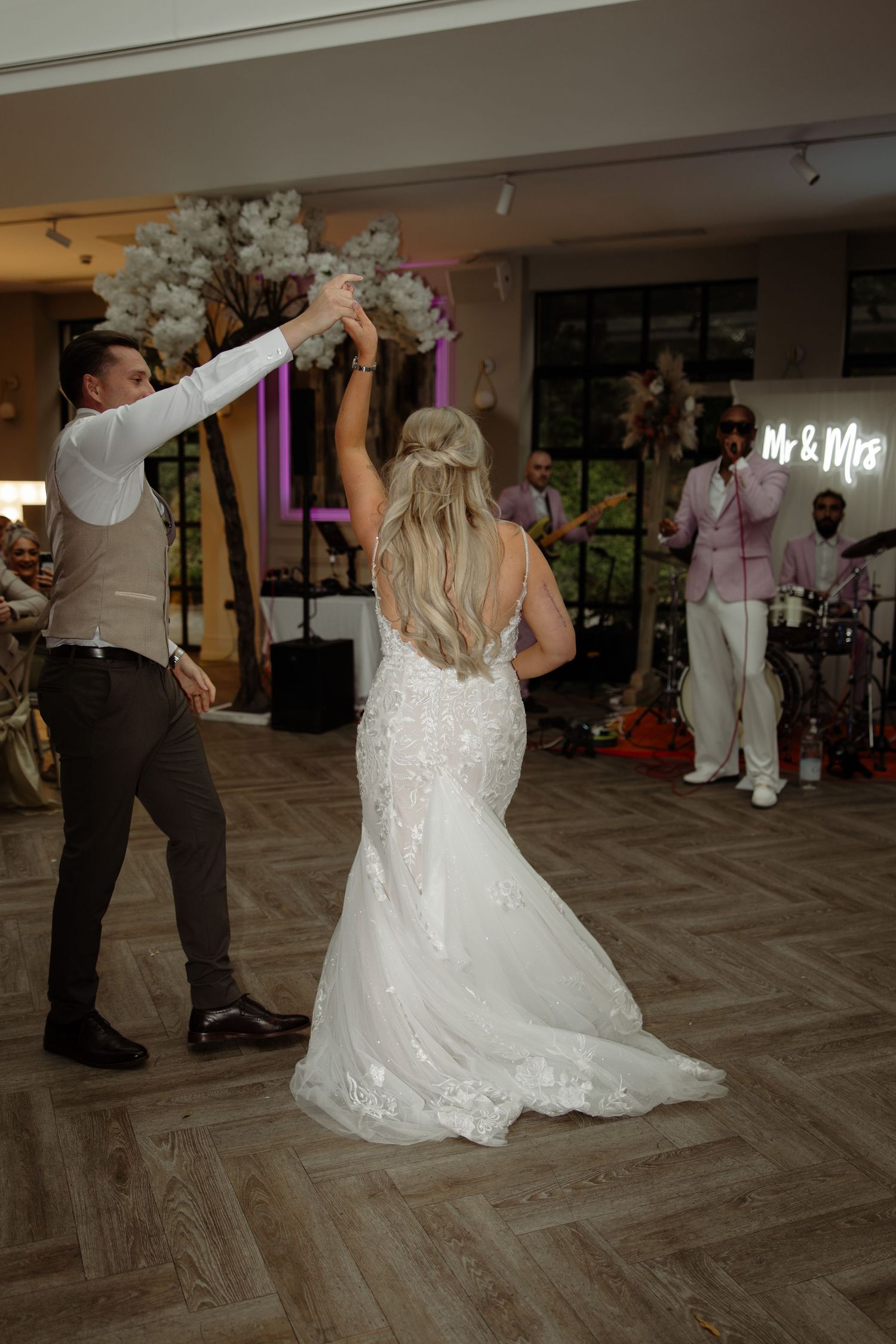 A couple dances together at a wedding reception on a gray patterned floor with white decor in the background.