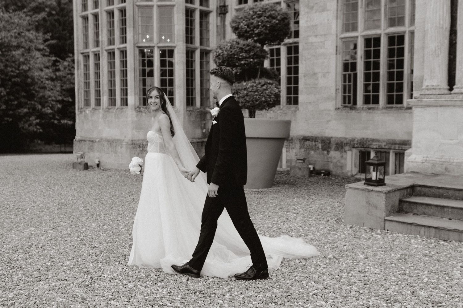 A romantic wedding couple walks together on gravel outside a historic mansion showing multiple perspectives.