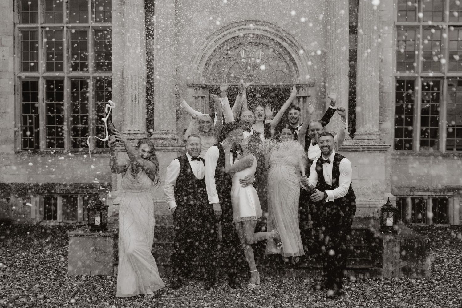 Wedding party celebrates with confetti in front of a historic stone church entrance in black and white photograph.