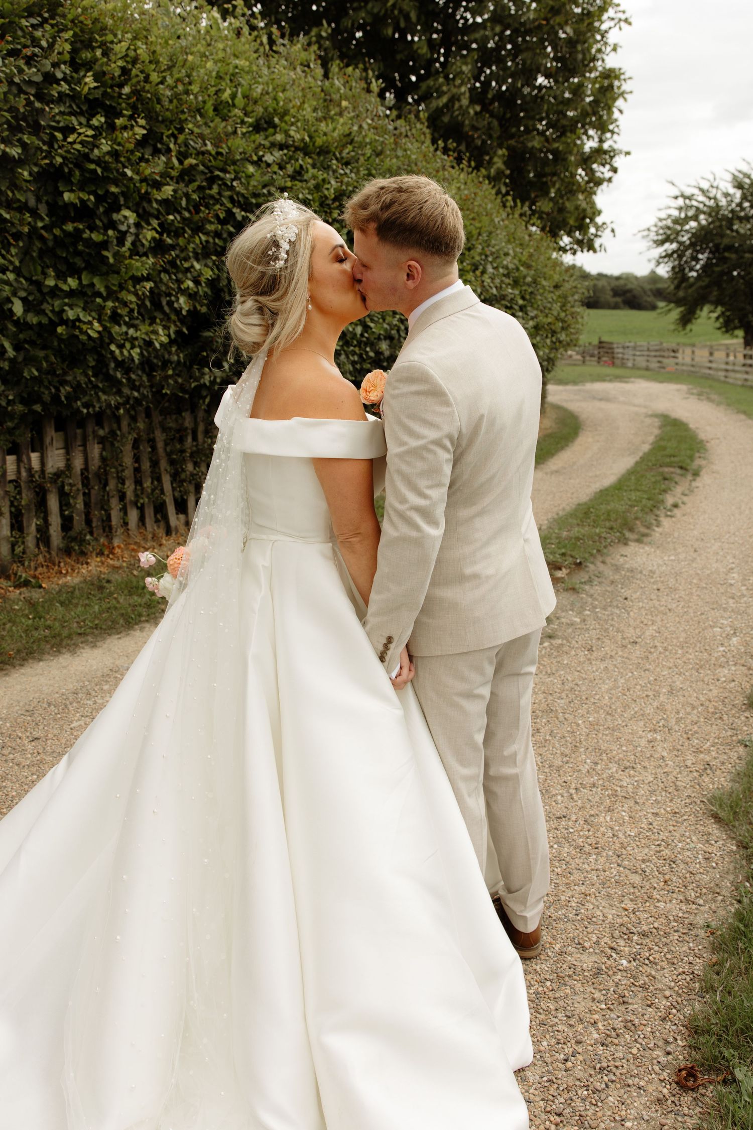 A couple in wedding attire walking together on a tree-lined gravel path, captured from different angles.
