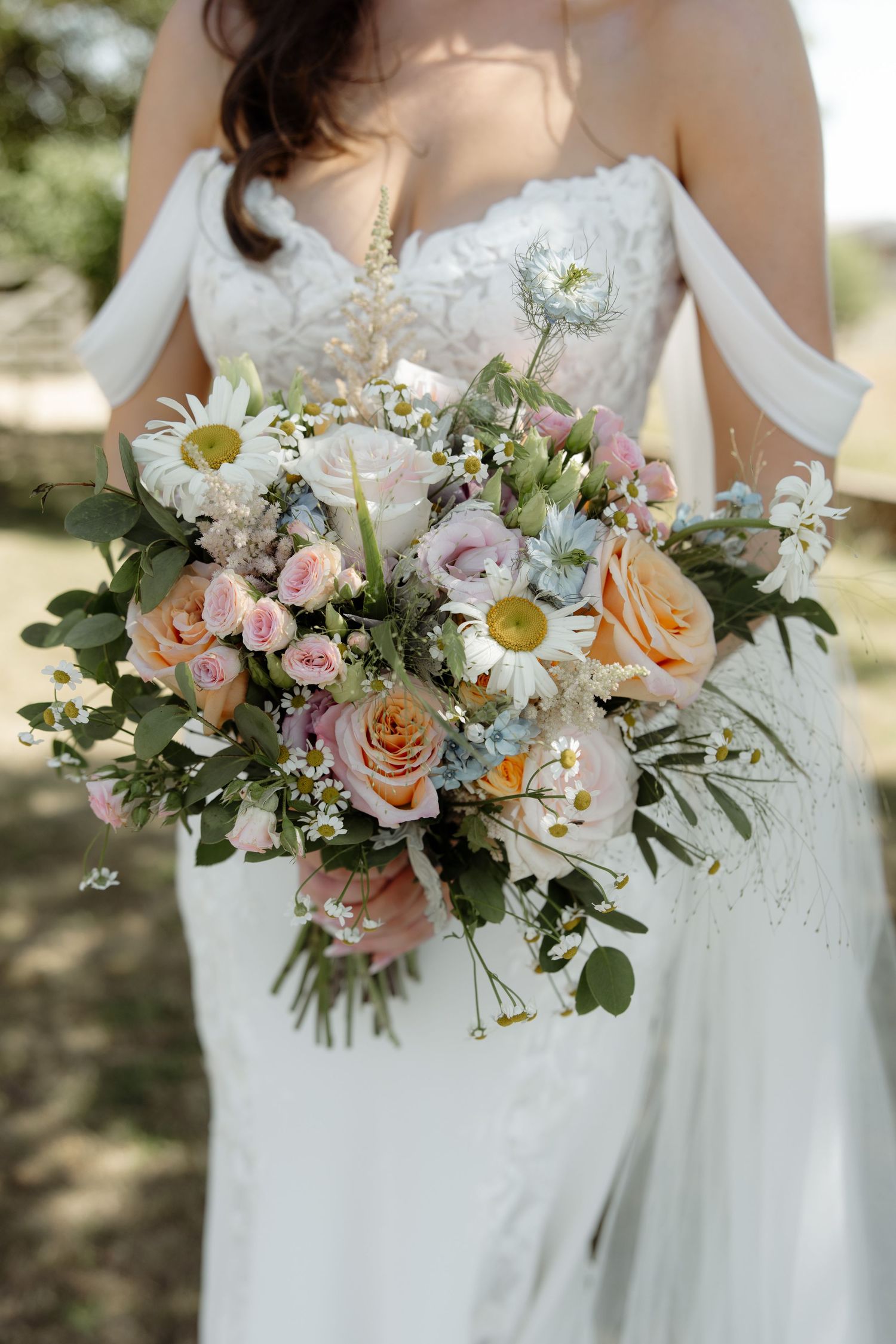 Elegant wedding bouquets featuring soft pink roses, white daisies, and greenery held against white bridal gowns.