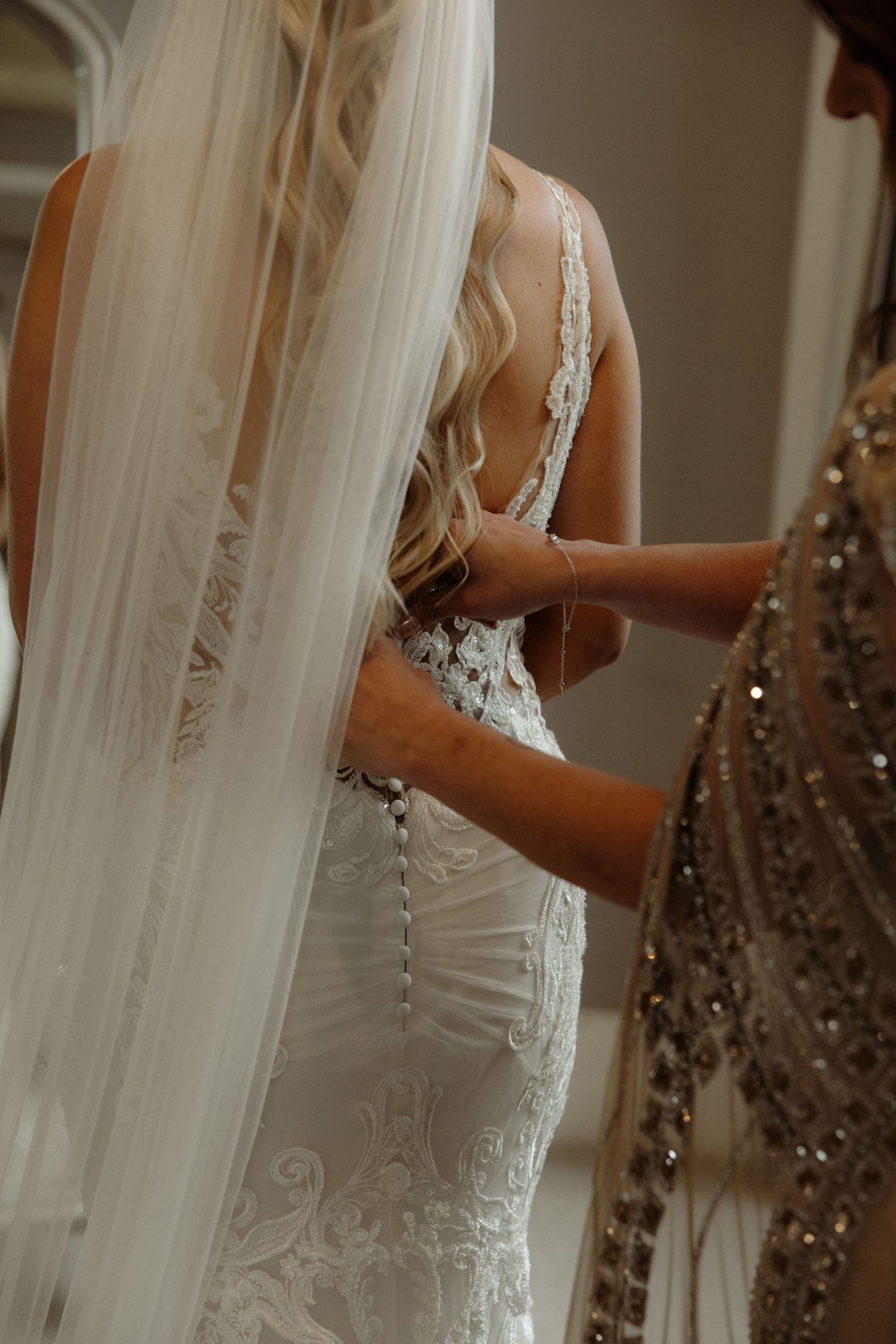 Close-up view of an elegant white lace wedding dress with delicate beading and flowing veil during final fitting.