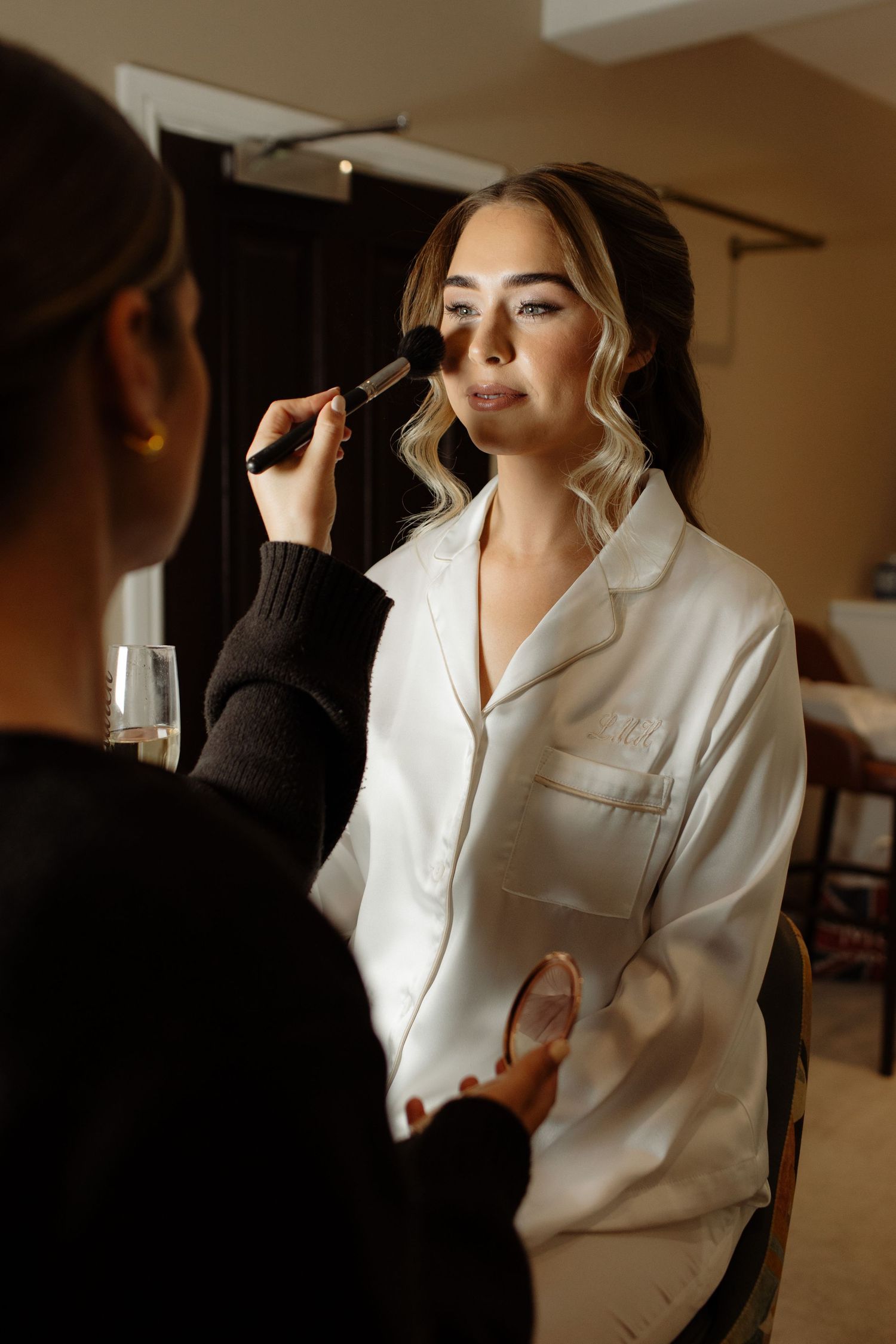 Makeup artist applying cosmetics in warm lighting during bridal preparation.