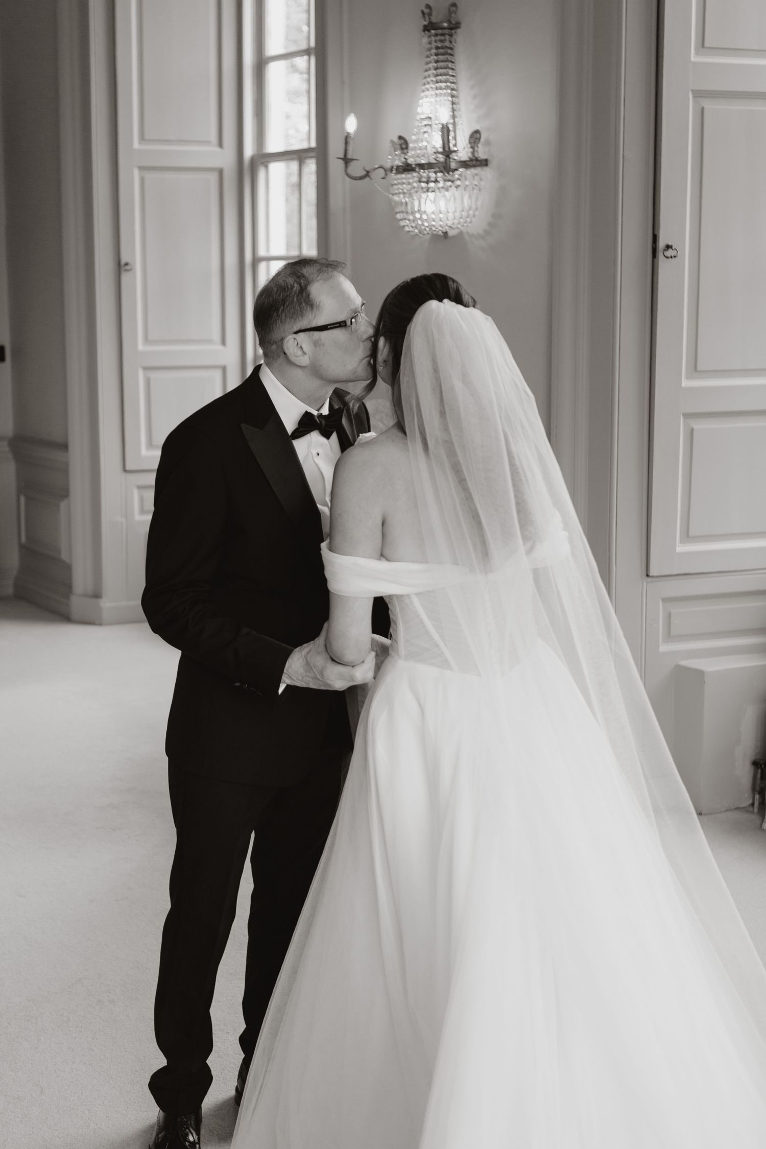 Elegant black and white wedding photos showing a bride in flowing gown with veil walking with groom in tuxedo.