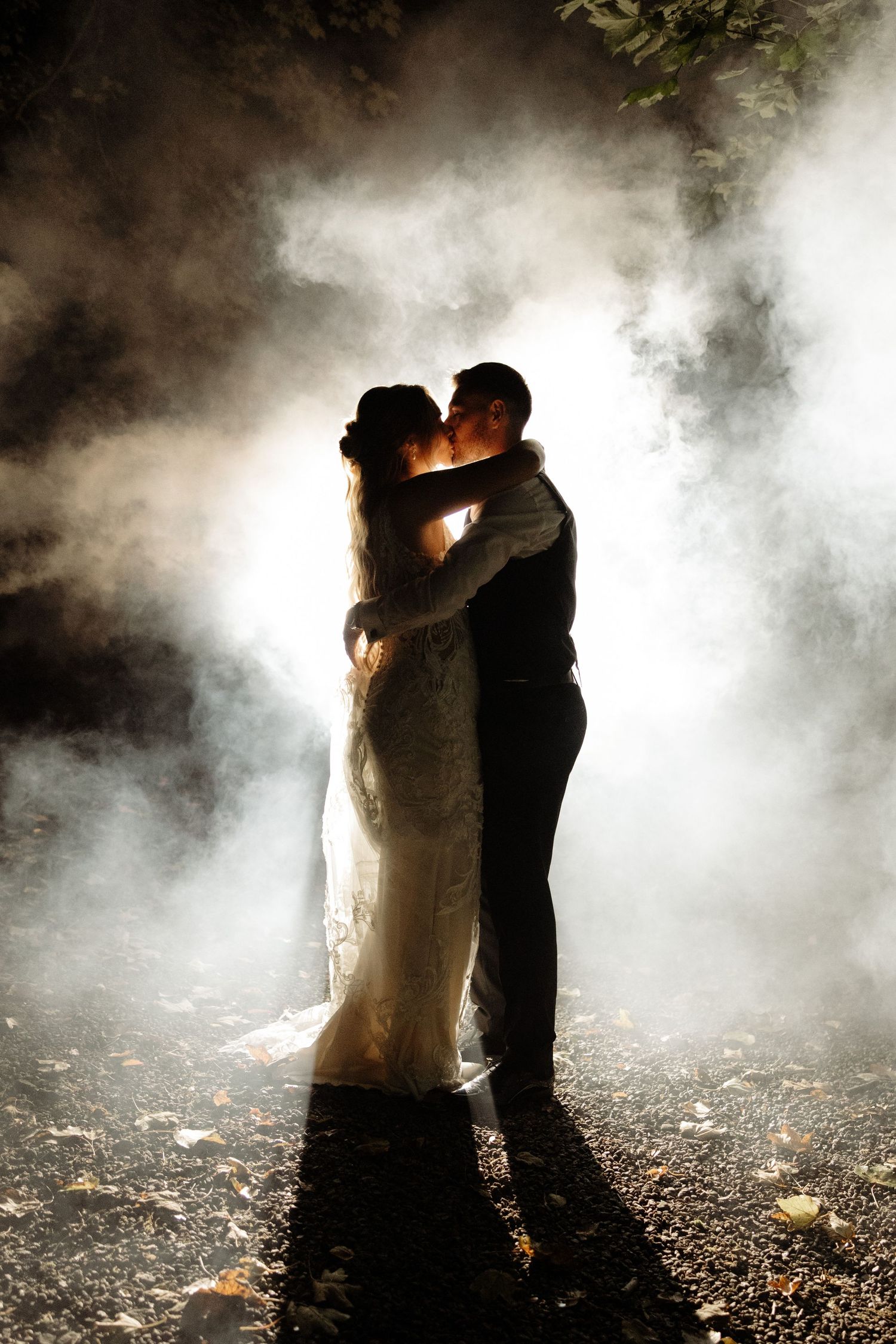 A silhouetted couple embraces in a misty forest setting with dramatic backlit fog creating a romantic atmosphere.