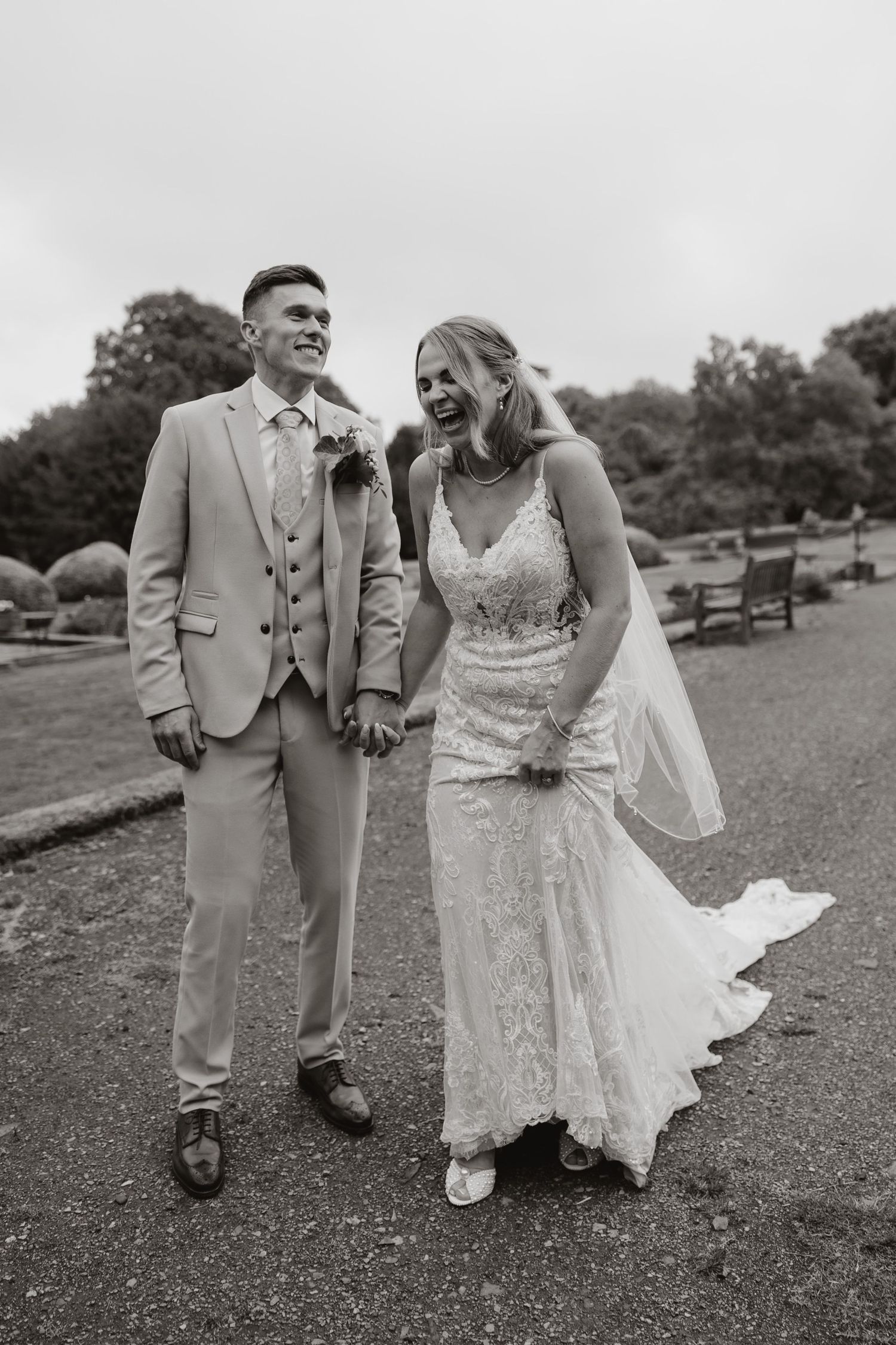 Black and white romantic wedding photo series showing couple walking together on grassy field in elegant attire.