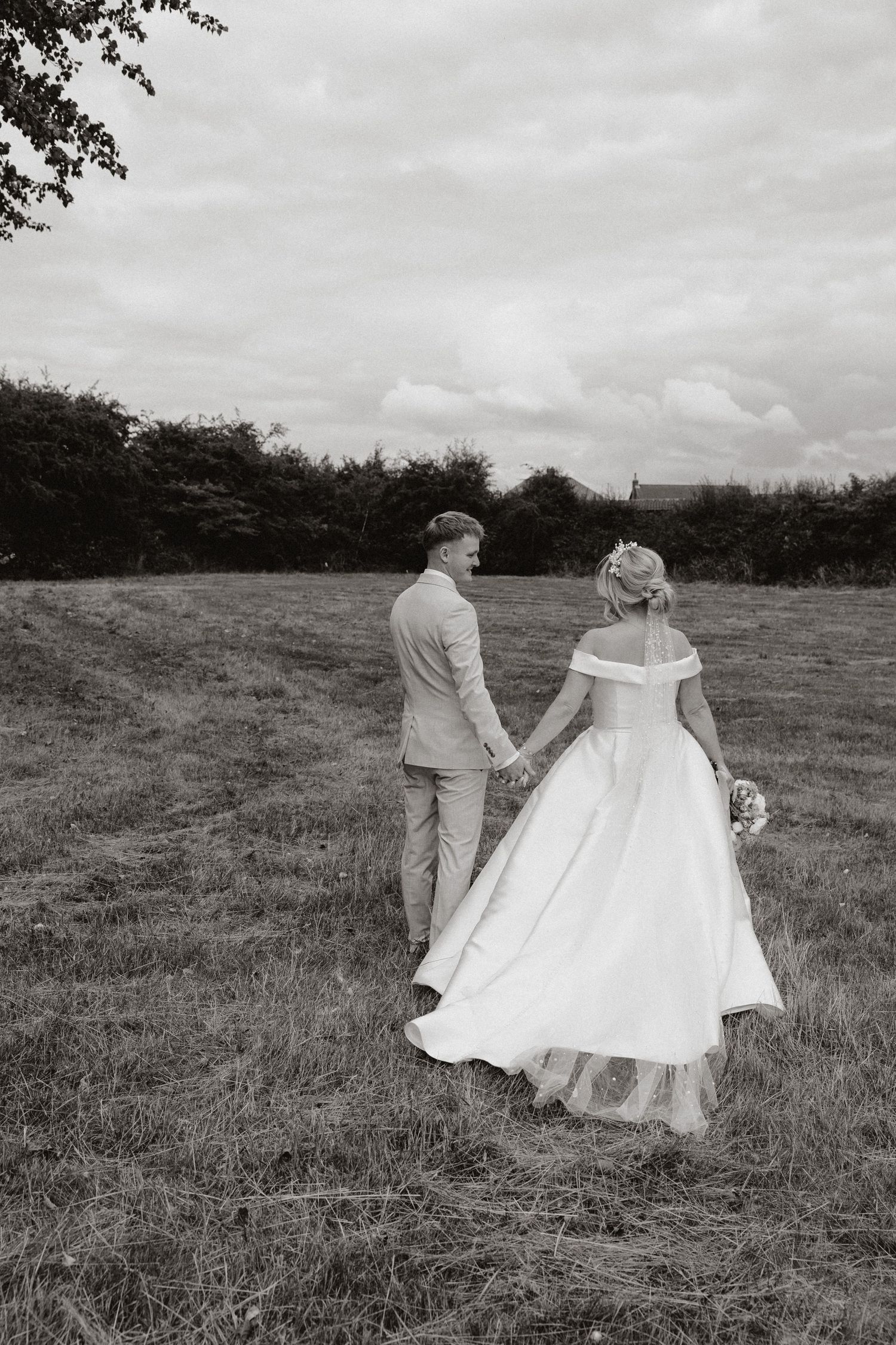 A wedding couple dances together in a rustic field under cloudy skies in black and white photography.