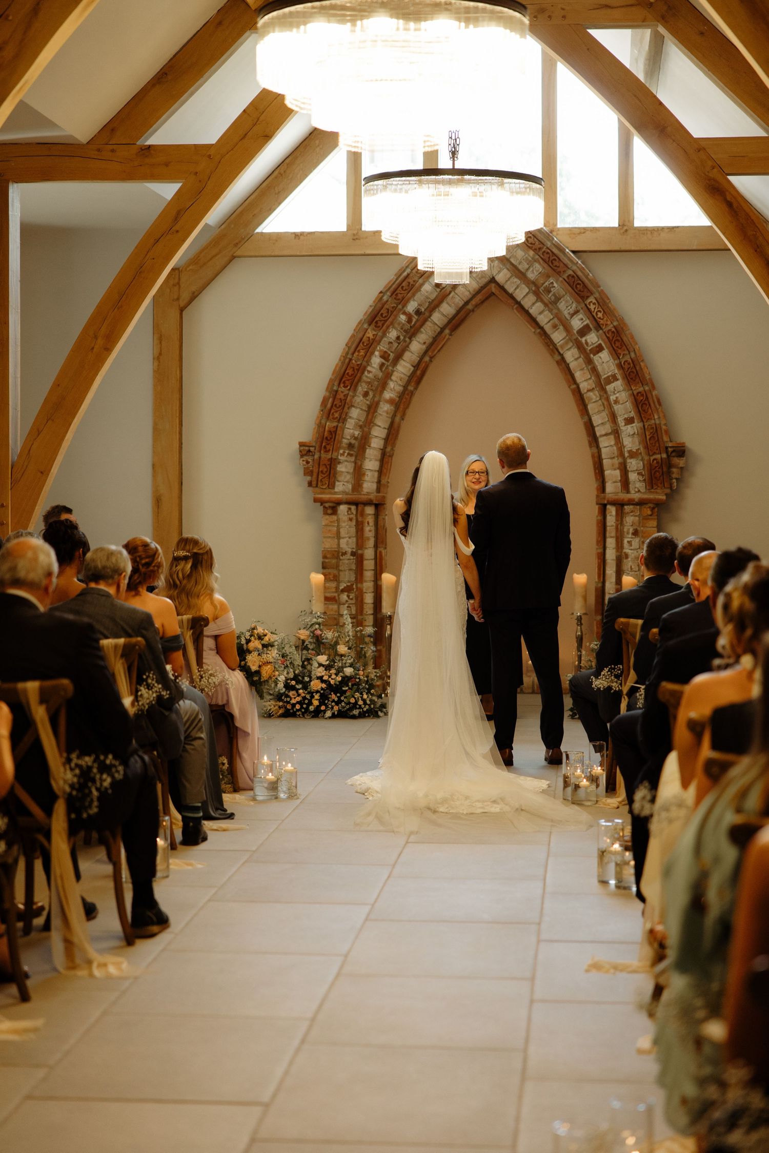 Panoramic view of a wedding ceremony in a rustic venue with exposed wooden beams and stone archways.