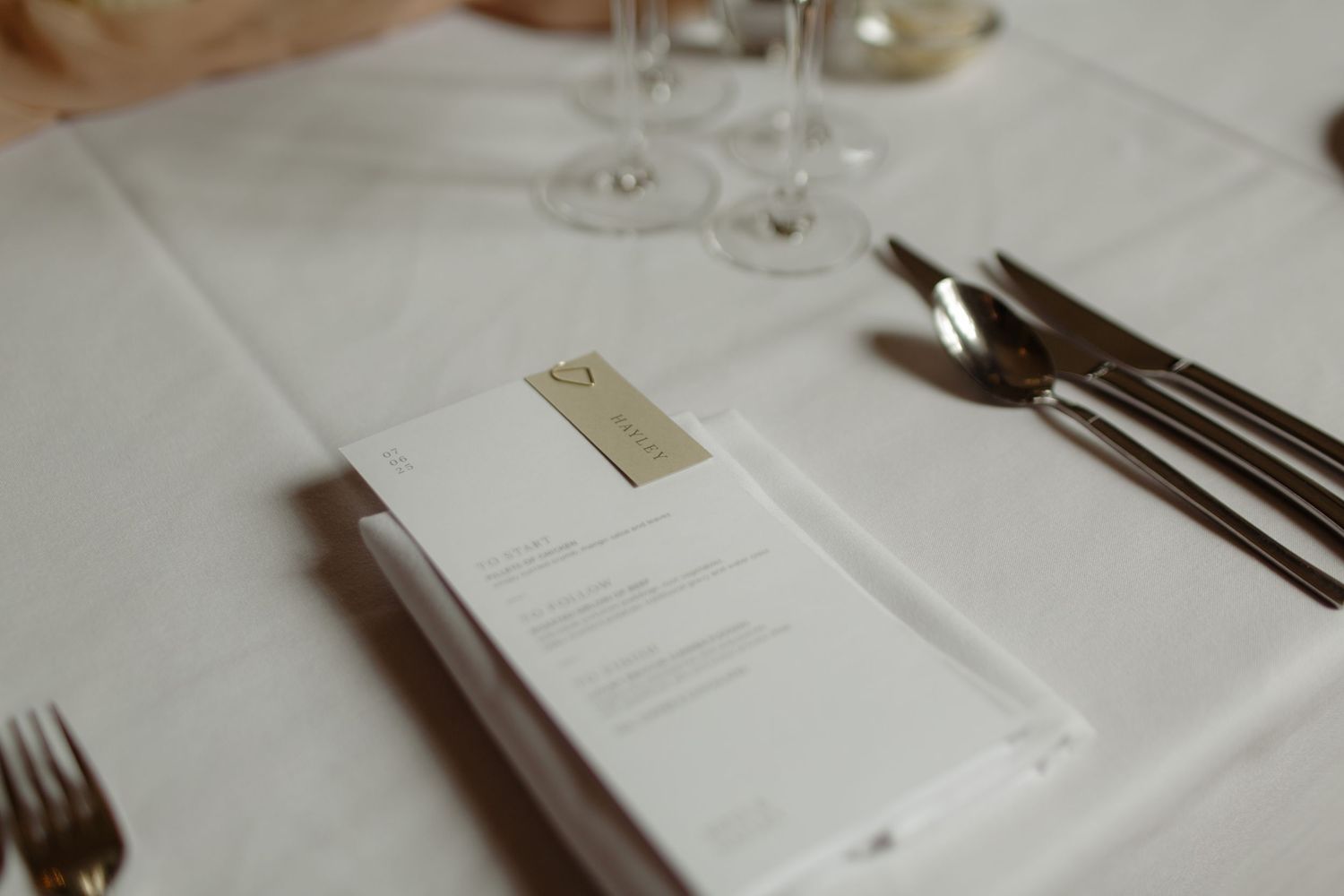 A detailed close-up view of an elegant white restaurant table setting with wine glasses and silverware.