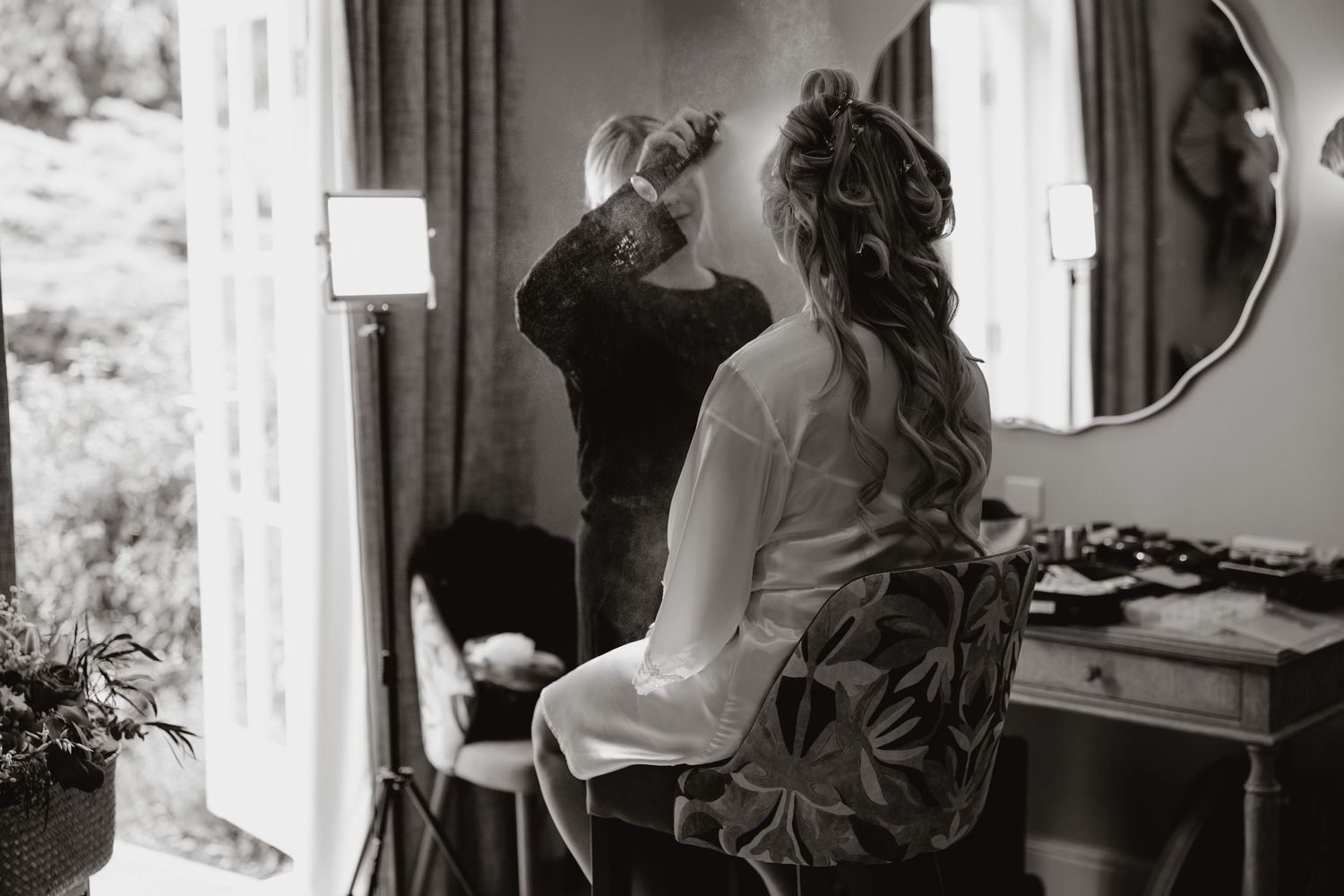 Black and white photo of someone getting ready at a vanity mirror on their wedding day.