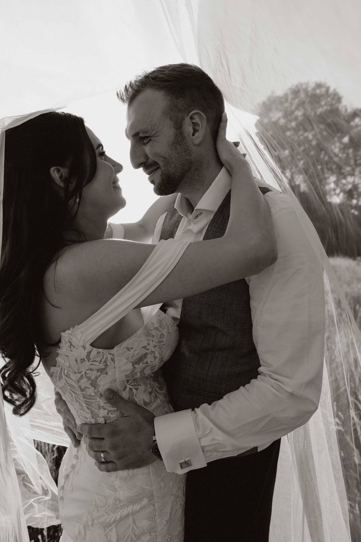 A romantic black and white wedding photo shows a couple embracing outdoors, with the bride in a lace dress and flowing veil.
