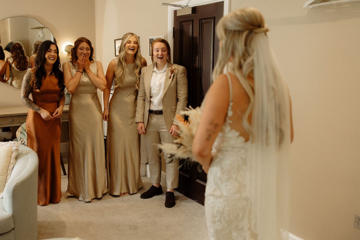 A wedding party shares an emotional moment with the bride in a room with cream-colored walls and elegant decor.