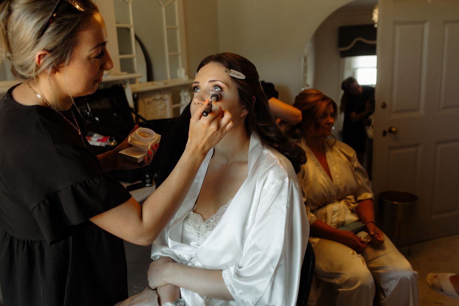 A sequence of photos shows someone in a white top being styled with makeup and hair products for a professional shoot.