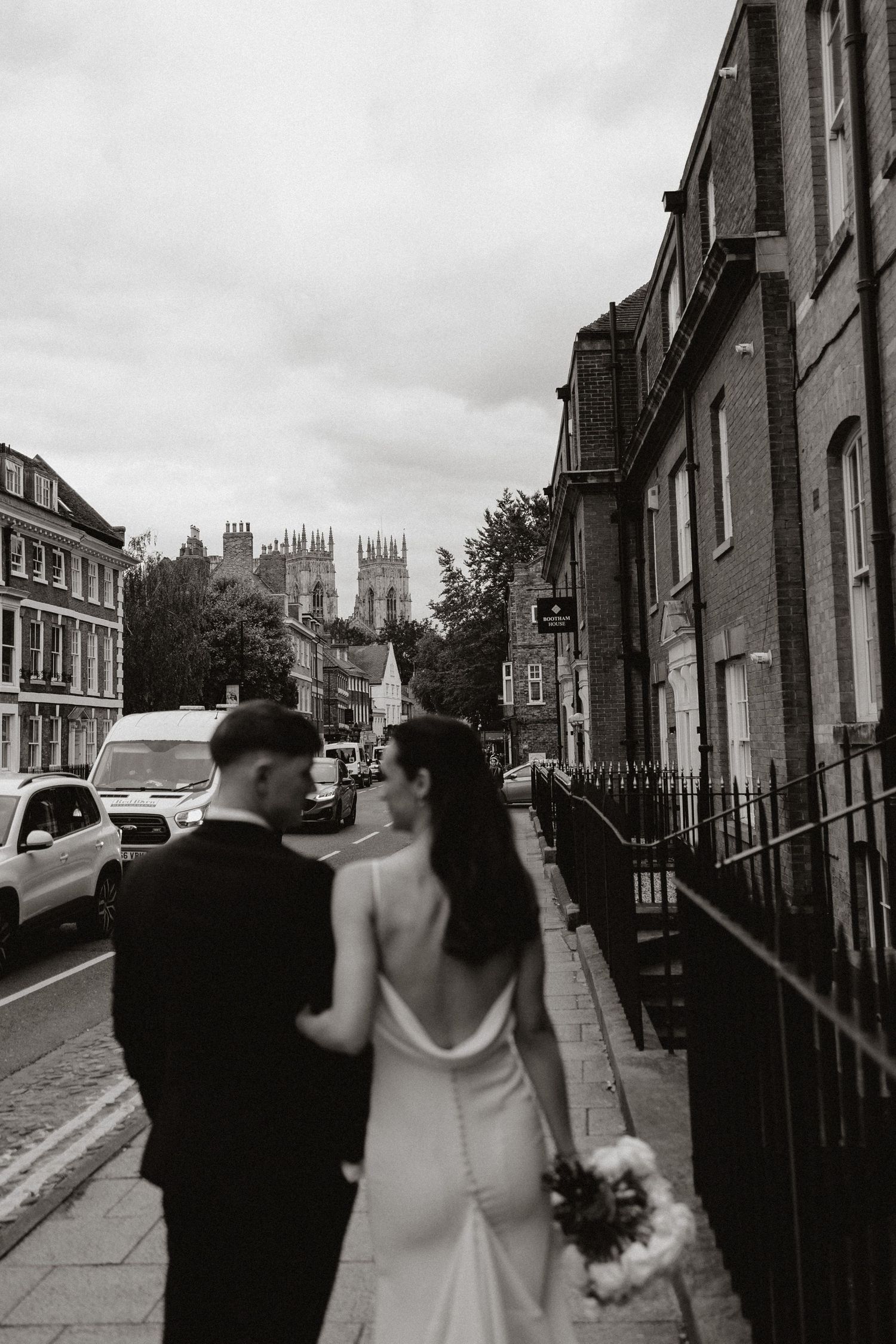 A couple walks down a historic street in York with cathedral spires visible in the distance.