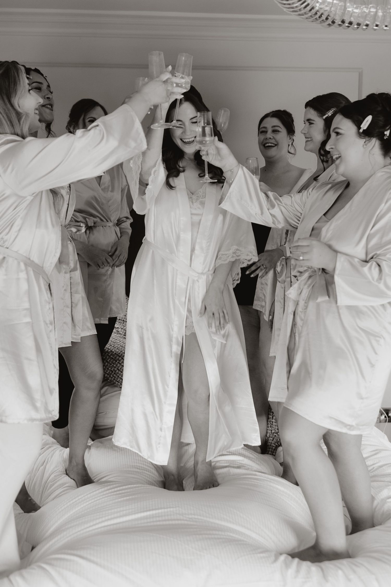 Multiple people wearing white clothing and sitting together on a bed in a playful black and white photograph.