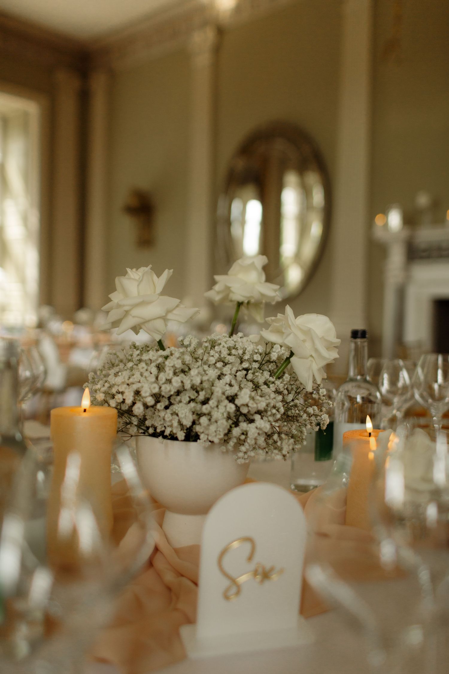 Elegant wedding reception table decor with white floral centerpieces and glowing candles in a luxurious banquet hall.