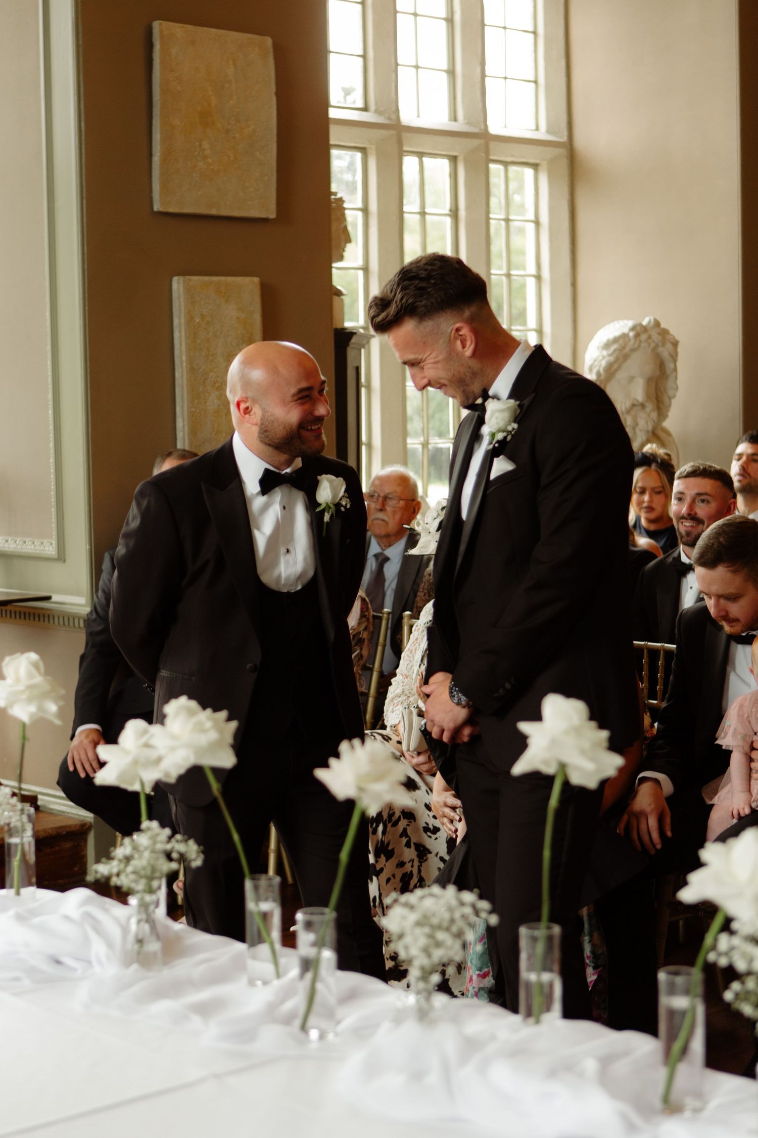 Guests bend over a table decorated with white flowers at a formal event.