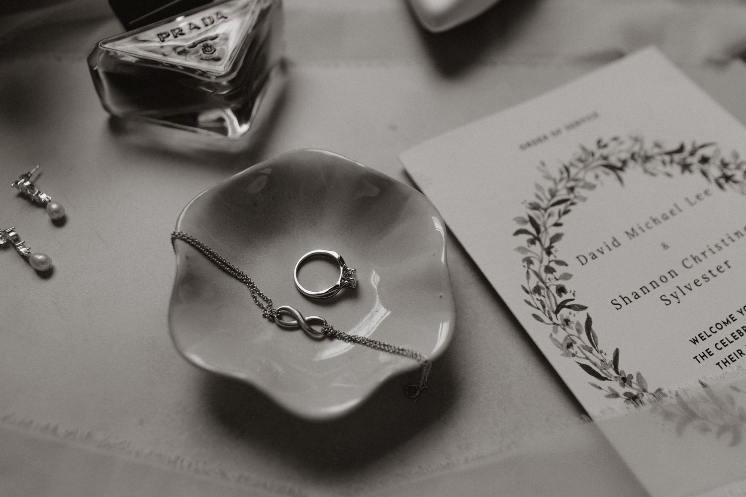 Wedding rings rest in a delicate white ceramic dish next to an invitation with floral wreath design.