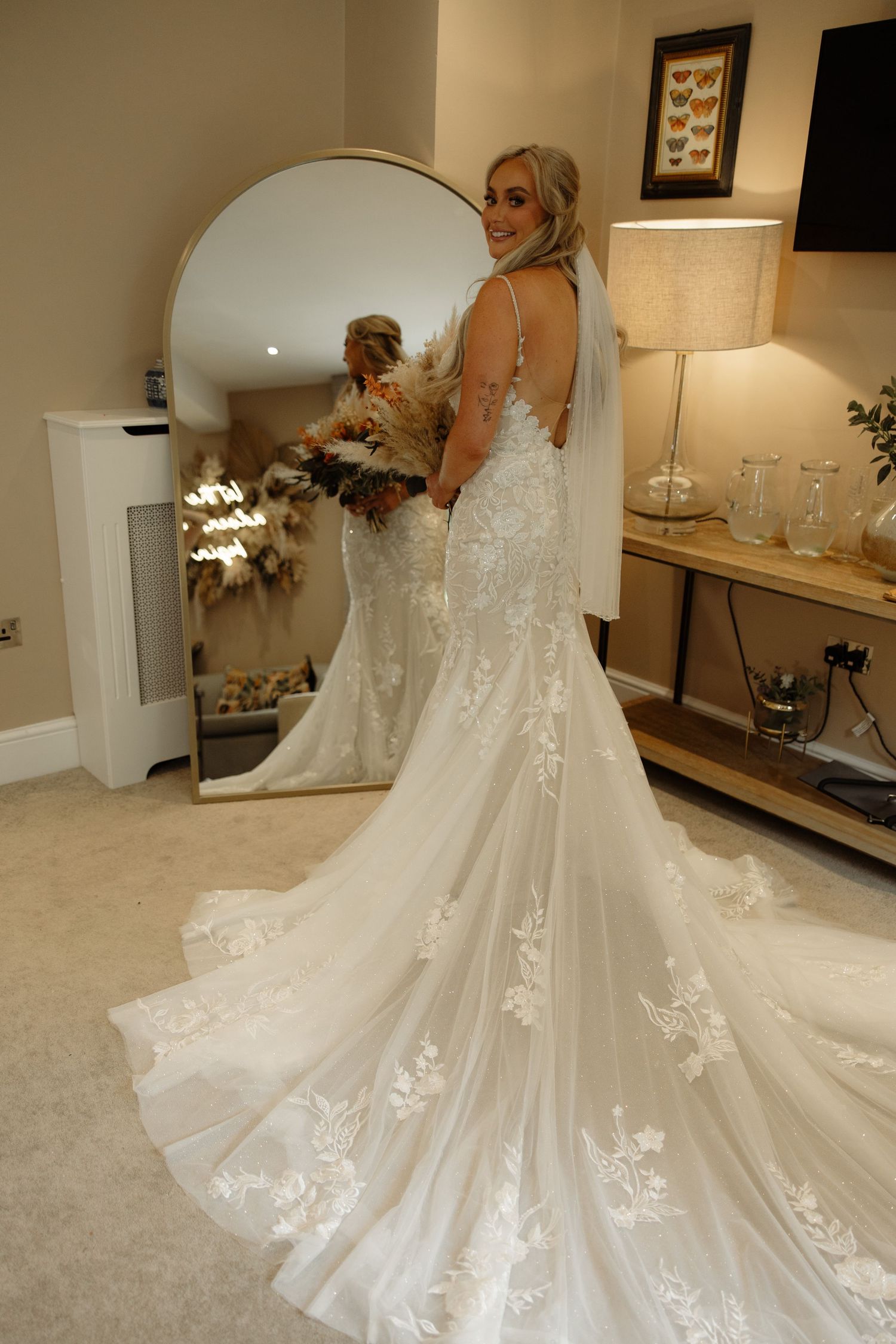 A stunning wedding dress with intricate lace details and a dramatic cathedral train displayed in a bridal fitting room.