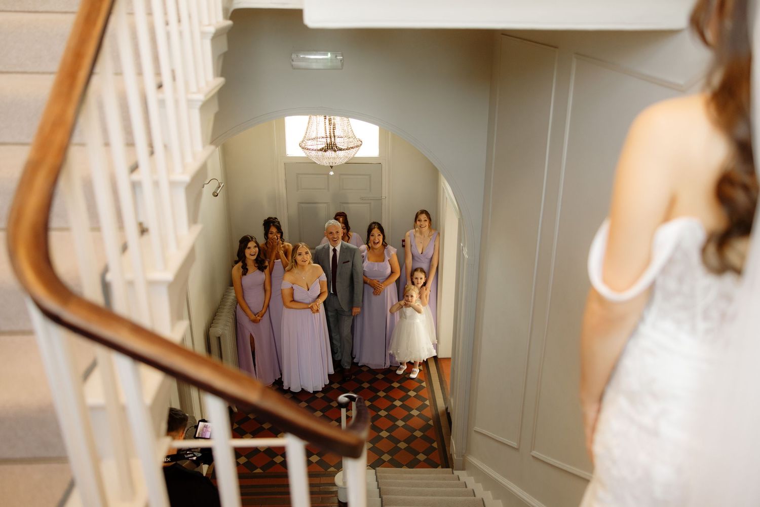 Bridesmaids in matching lavender dresses stand together on a staircase during a wedding celebration.