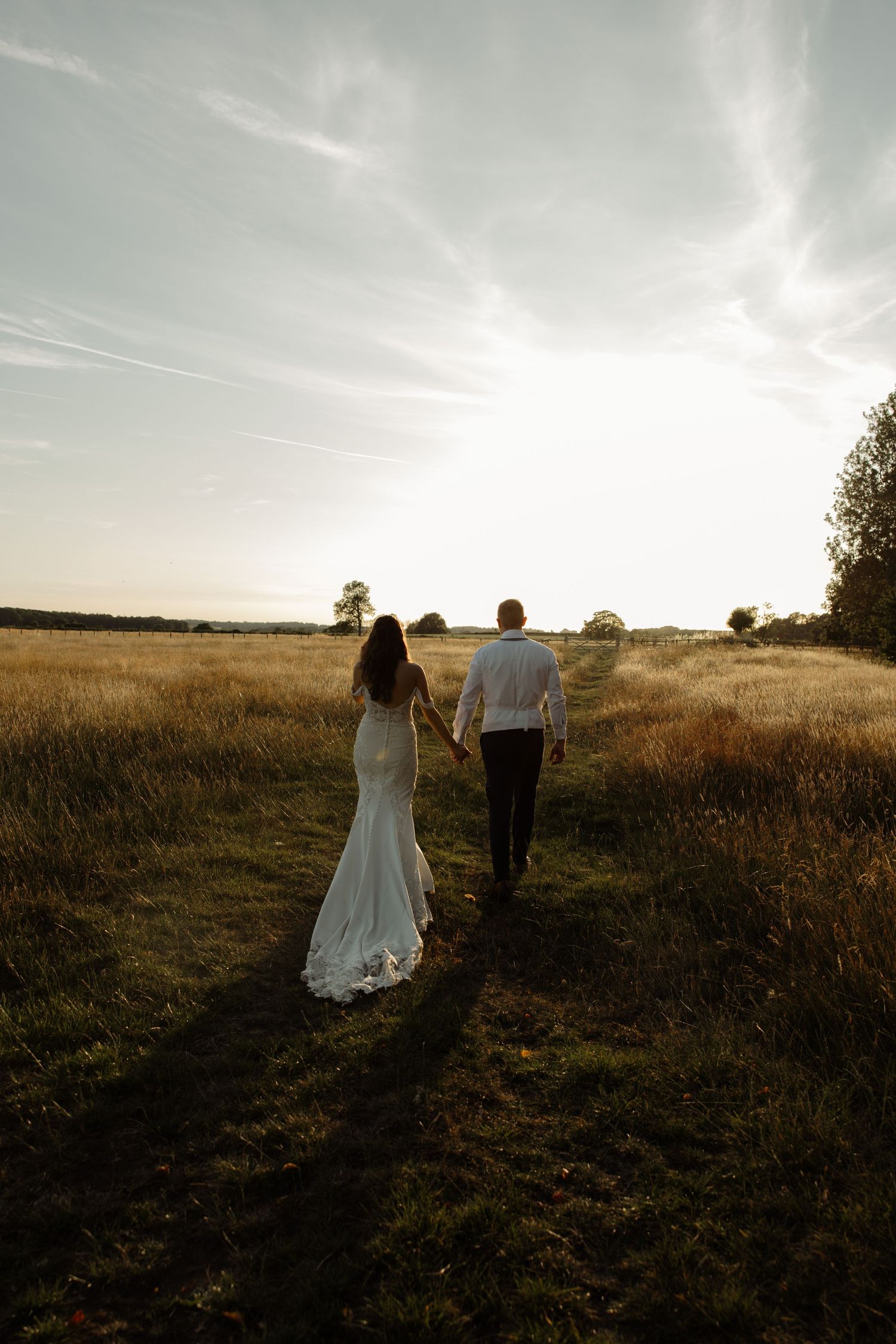 Two figures walk hand in hand through a golden sunset meadow while cast in dramatic silhouettes against the evening sky.